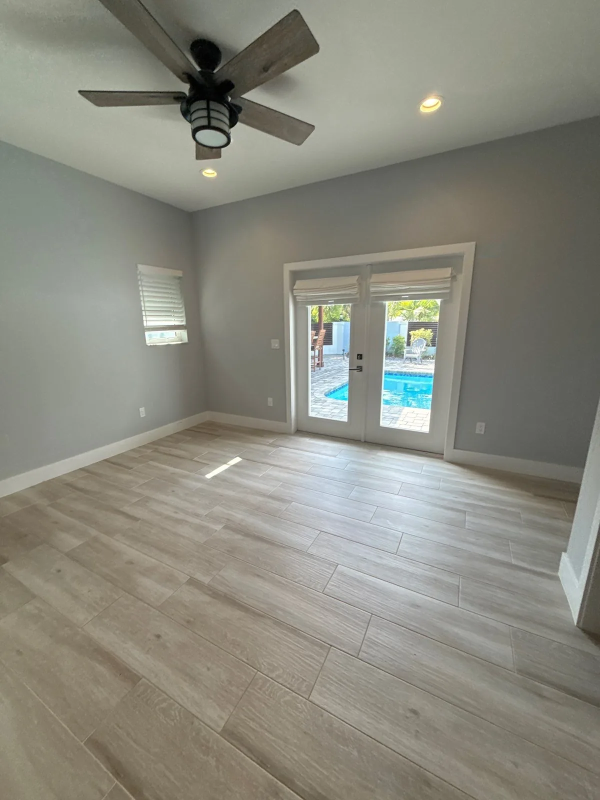 Interior Painting in North River Shores, Florida. Empty room with grey painted walls and white trim, ceiling fan, and French doors opening to a pool.