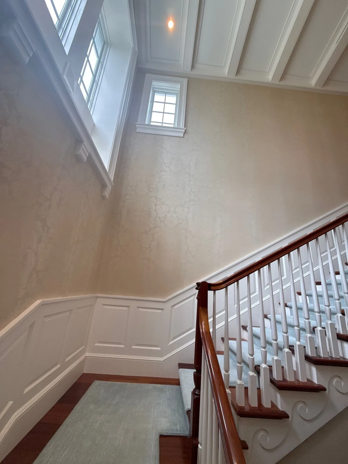 Interior Painting in Palm Beach, Florida. Stairwell with cream textured walls, white raised-panel wainscoting and white balustrade beneath a tall window.