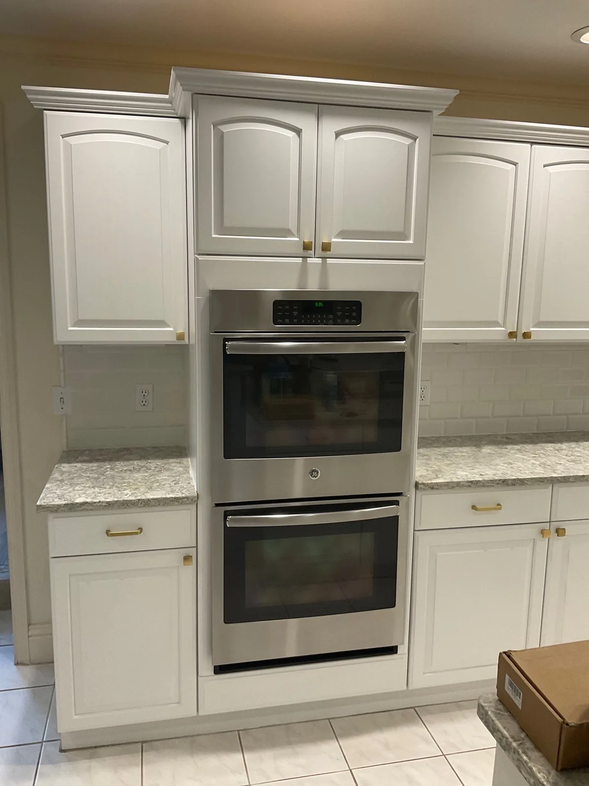 Cabinet Refinishing in Palm City, Florida. Refinished white cabinetry surrounding a stainless steel double wall oven, with crown moulding and stone countertops.