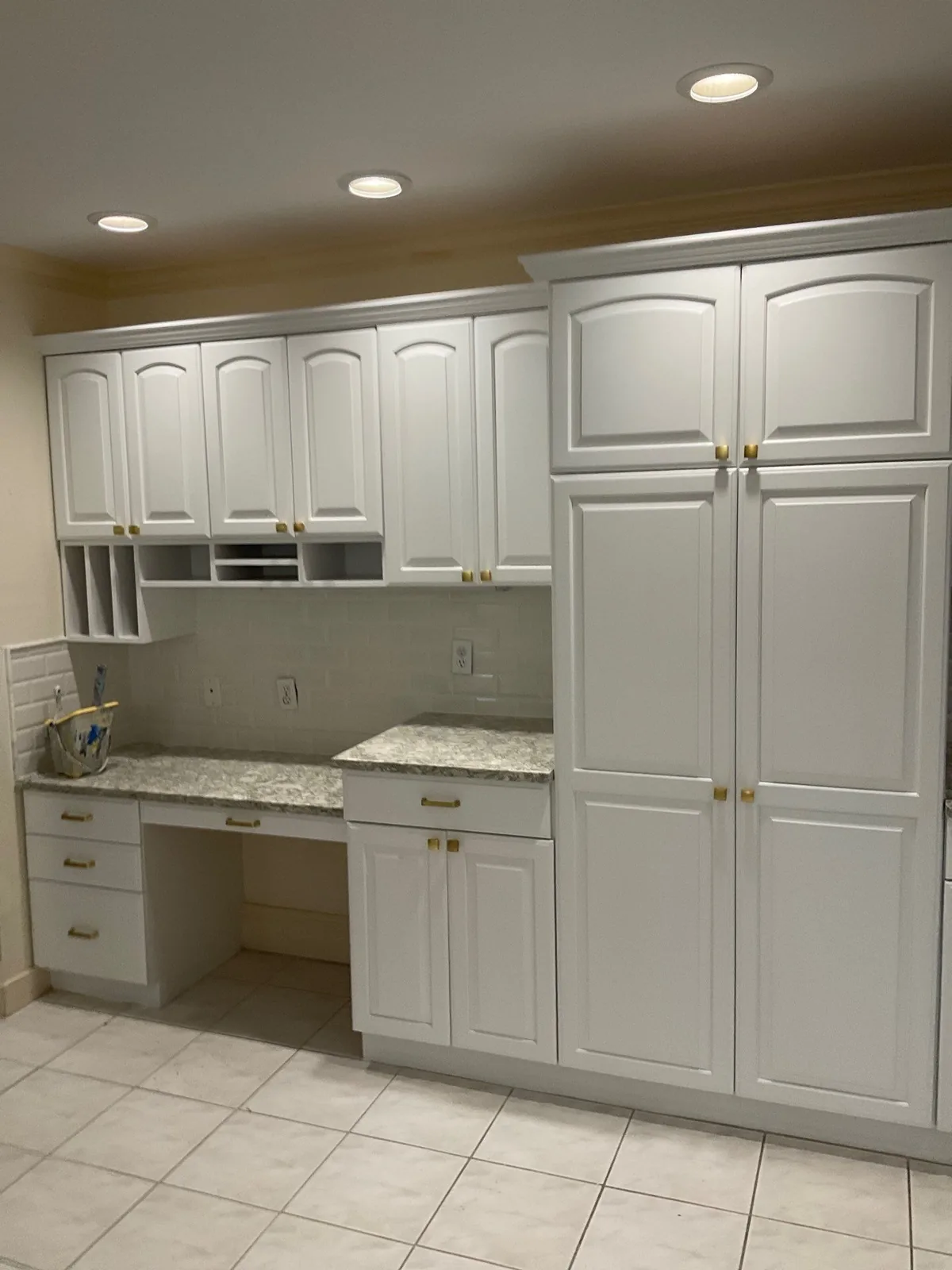 Cabinet Refinishing in Palm City, Florida. Refinished white raised-panel cabinetry with a built-in desk nook, a tall pantry cabinet, granite countertops and brass knobs.