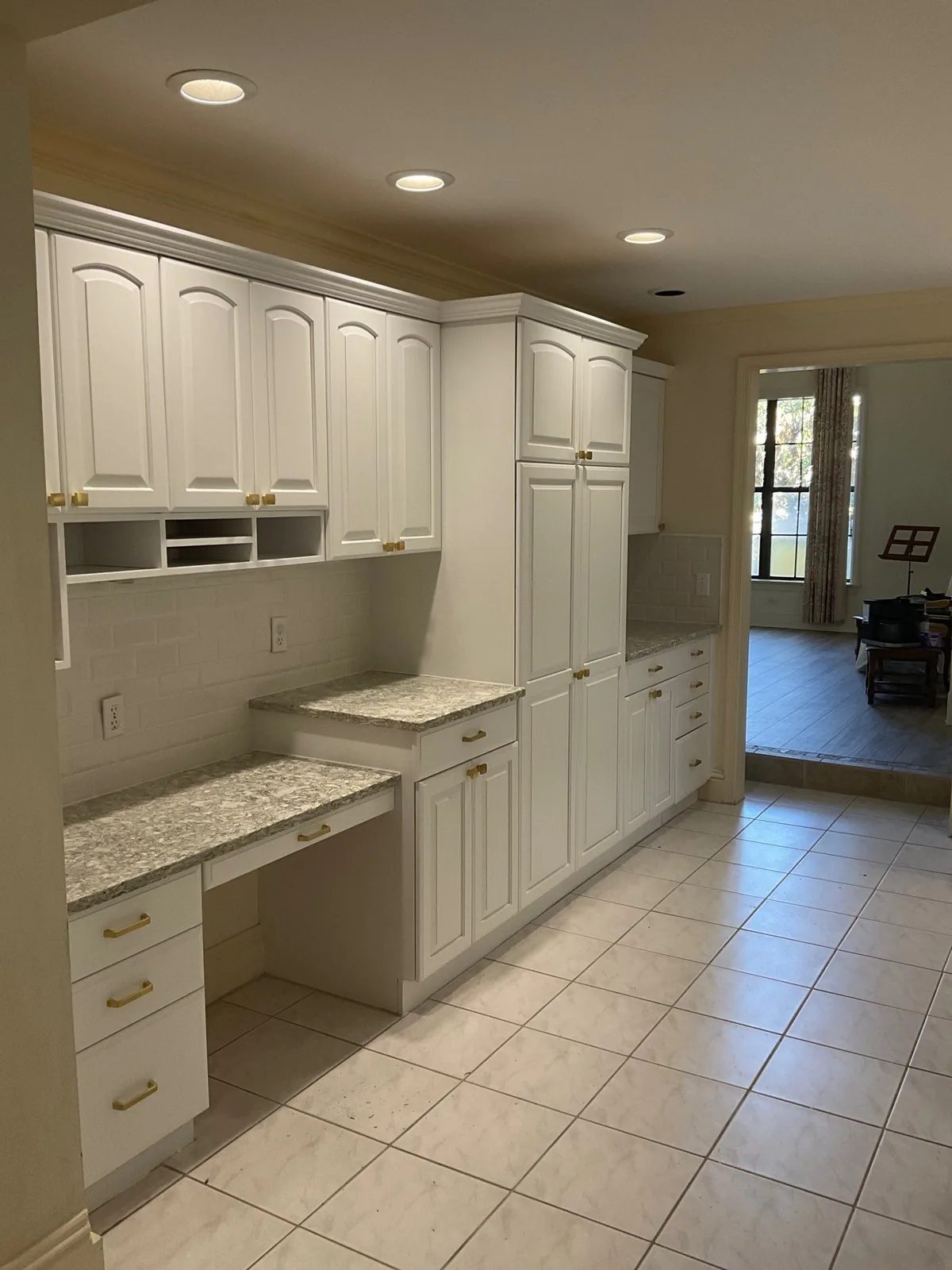 Cabinet Refinishing in Palm City, Florida. Wide view of a finished white cabinet run with desk area and granite counters, tile floor leading to a glass door.