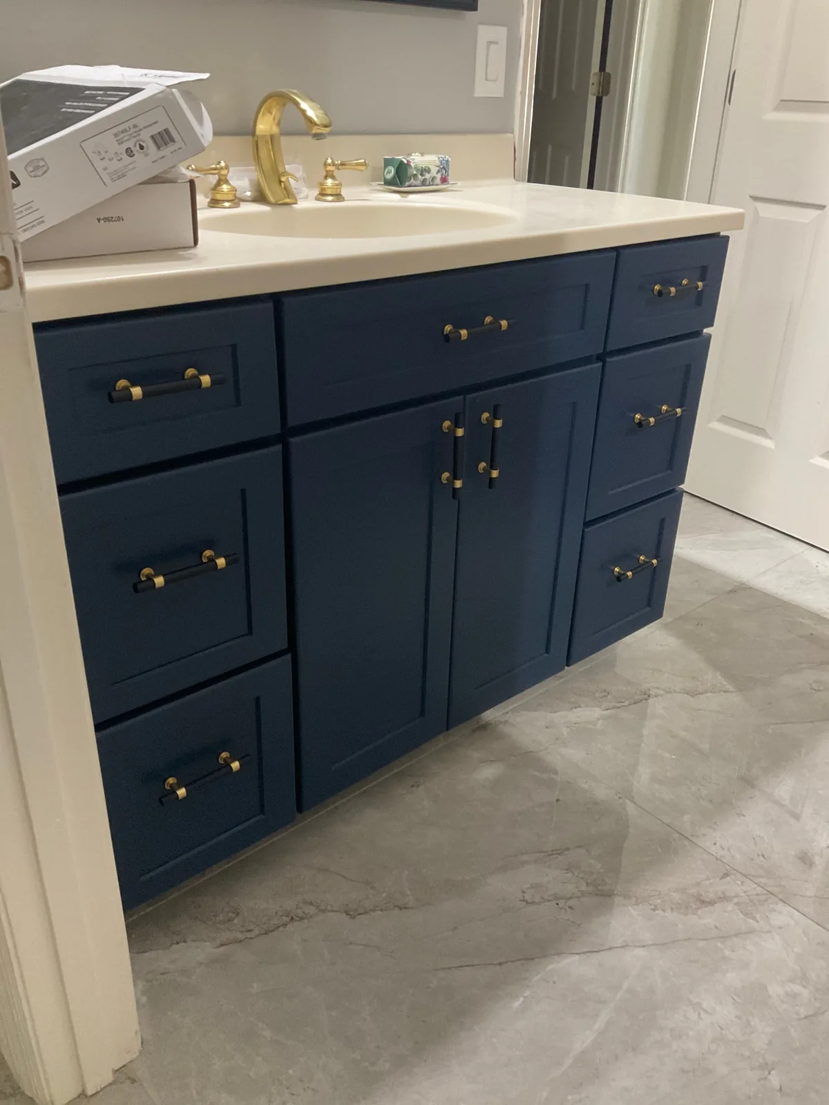 Cabinet Refinishing in Palm City, Florida. Refinished bathroom vanity painted navy blue with brass bar pulls, white countertop and gold widespread faucet.