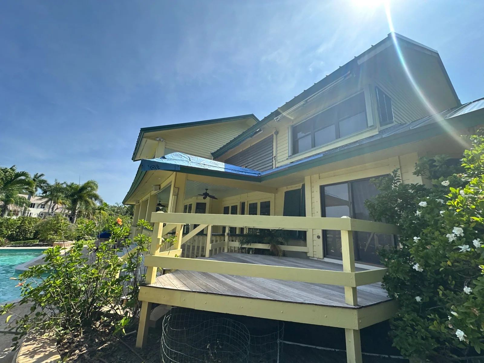 Exterior Painting in Palm City, Florida. Two-storey yellow house with white railings and a raised deck, seen from beside the pool.