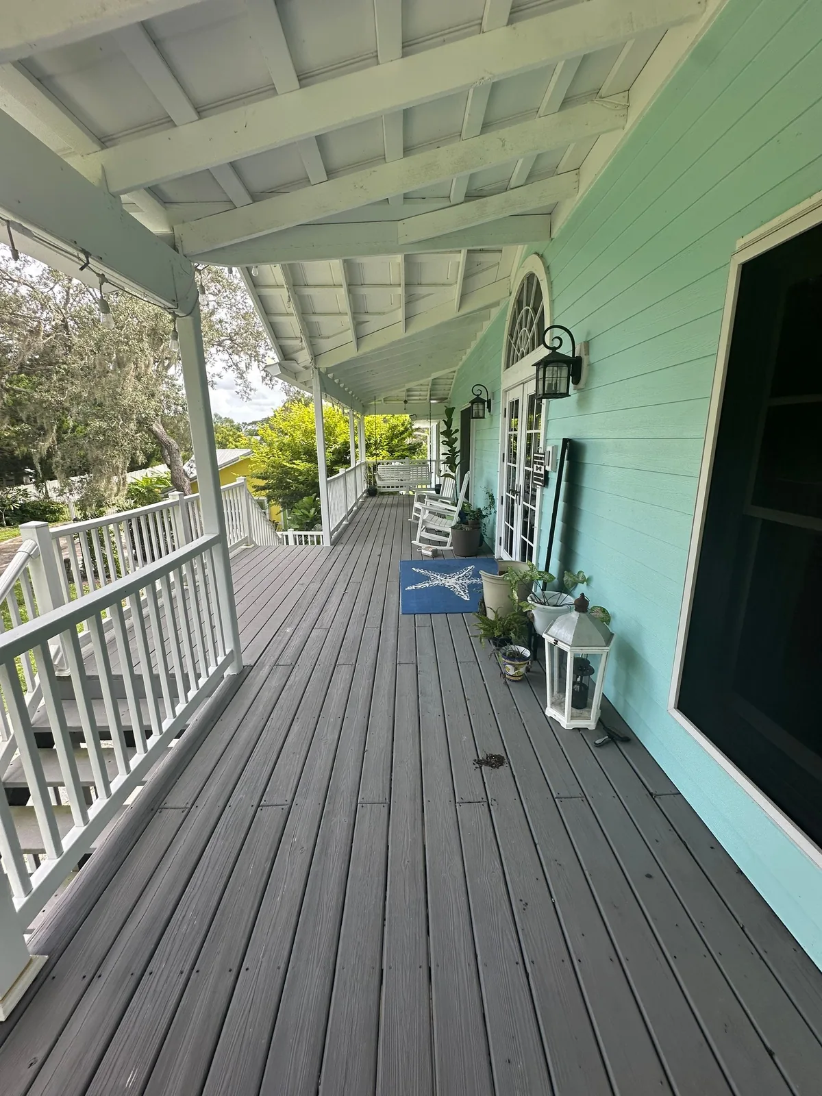 Exterior Painting in Palm City, Florida. Covered wraparound porch with mint green lap siding, white railings and columns, and a grey painted deck.