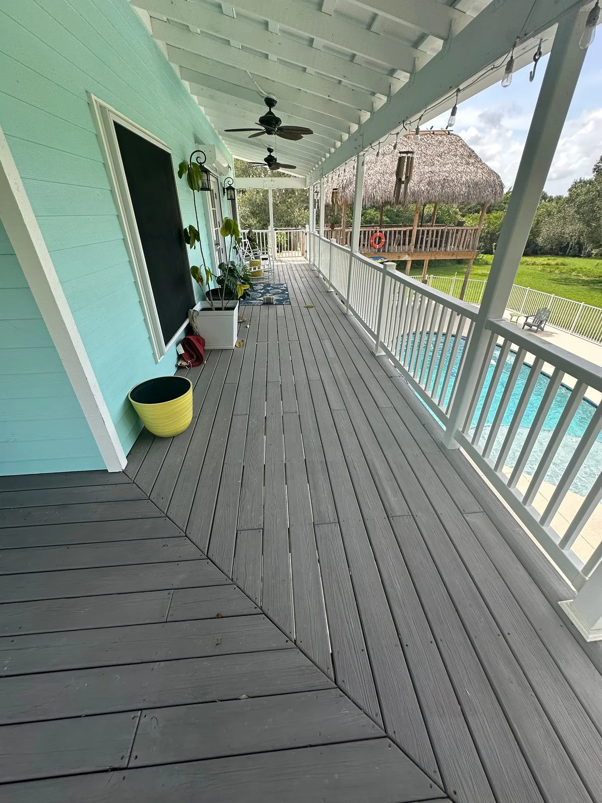 Exterior Painting in Palm City, Florida. Porch with mint green siding, white ceiling and railings, grey painted decking, pool and thatched cabana beyond.
