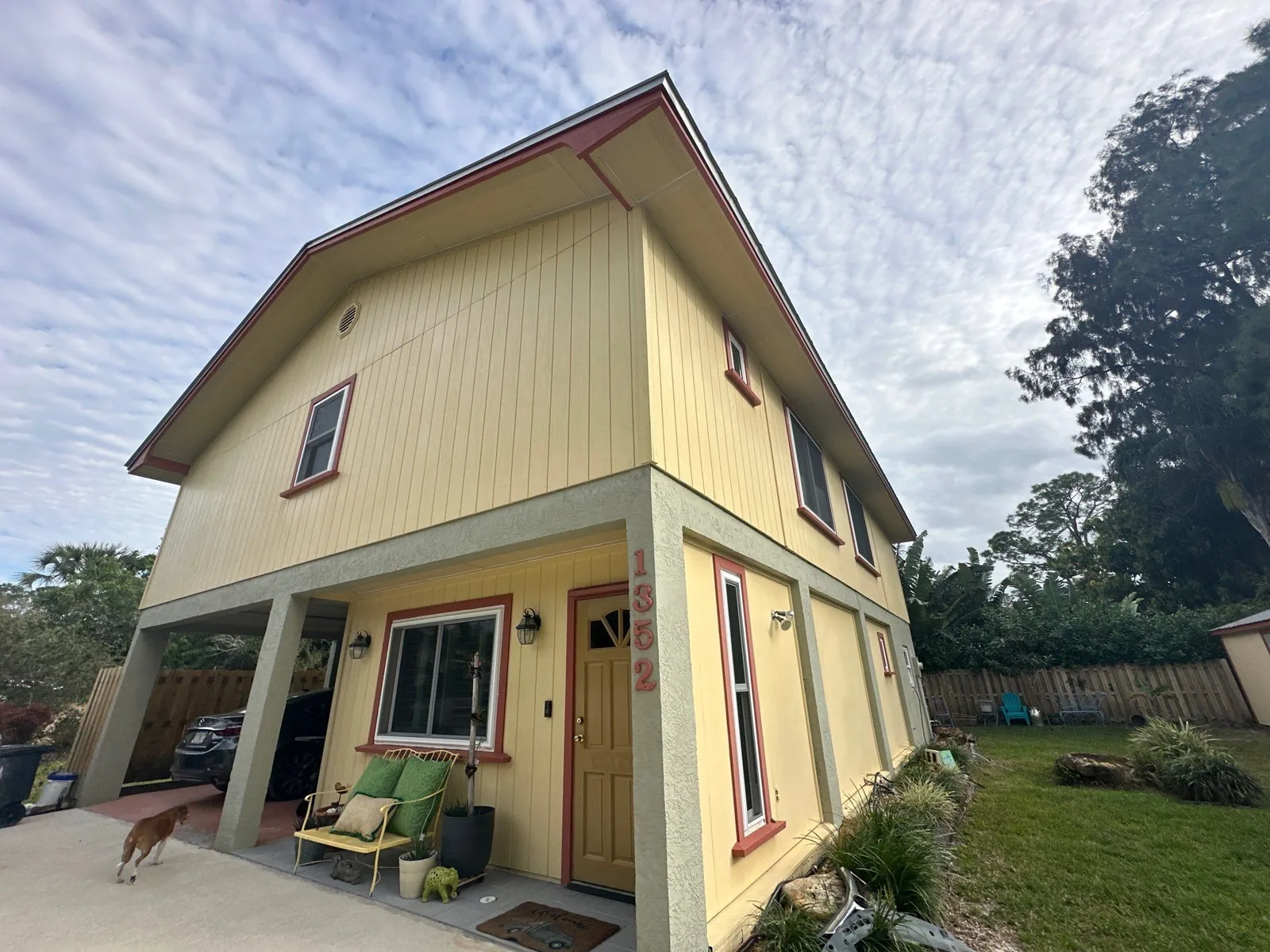 Exterior Painting in Palm City, Florida. Two-storey yellow board-and-batten house with dark red trim and a covered front porch, shot in daylight.