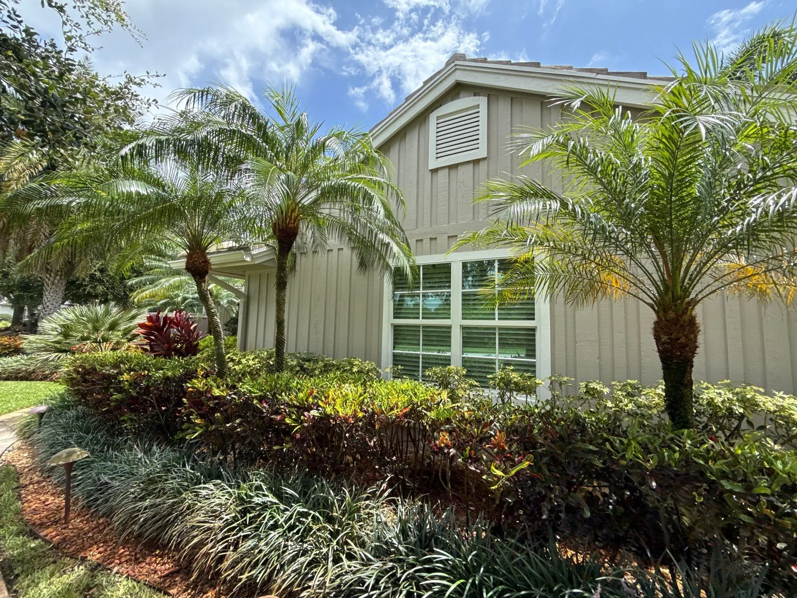 Exterior Painting in Palm City, Florida. Single-storey home exterior with beige board-and-batten siding, white-trimmed picture window and gable vent.