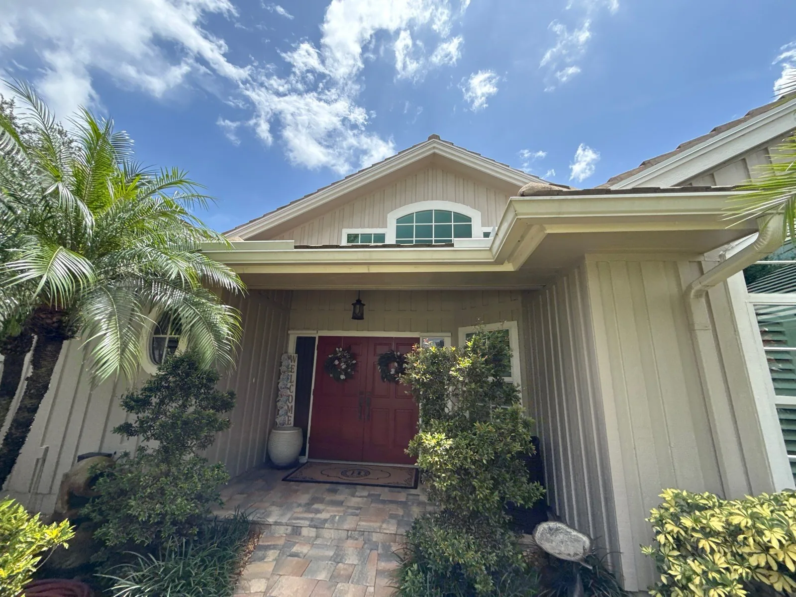 Exterior Painting in Palm City, Florida. Covered front entry of a home with beige siding, white gable trim and a red panelled front door.