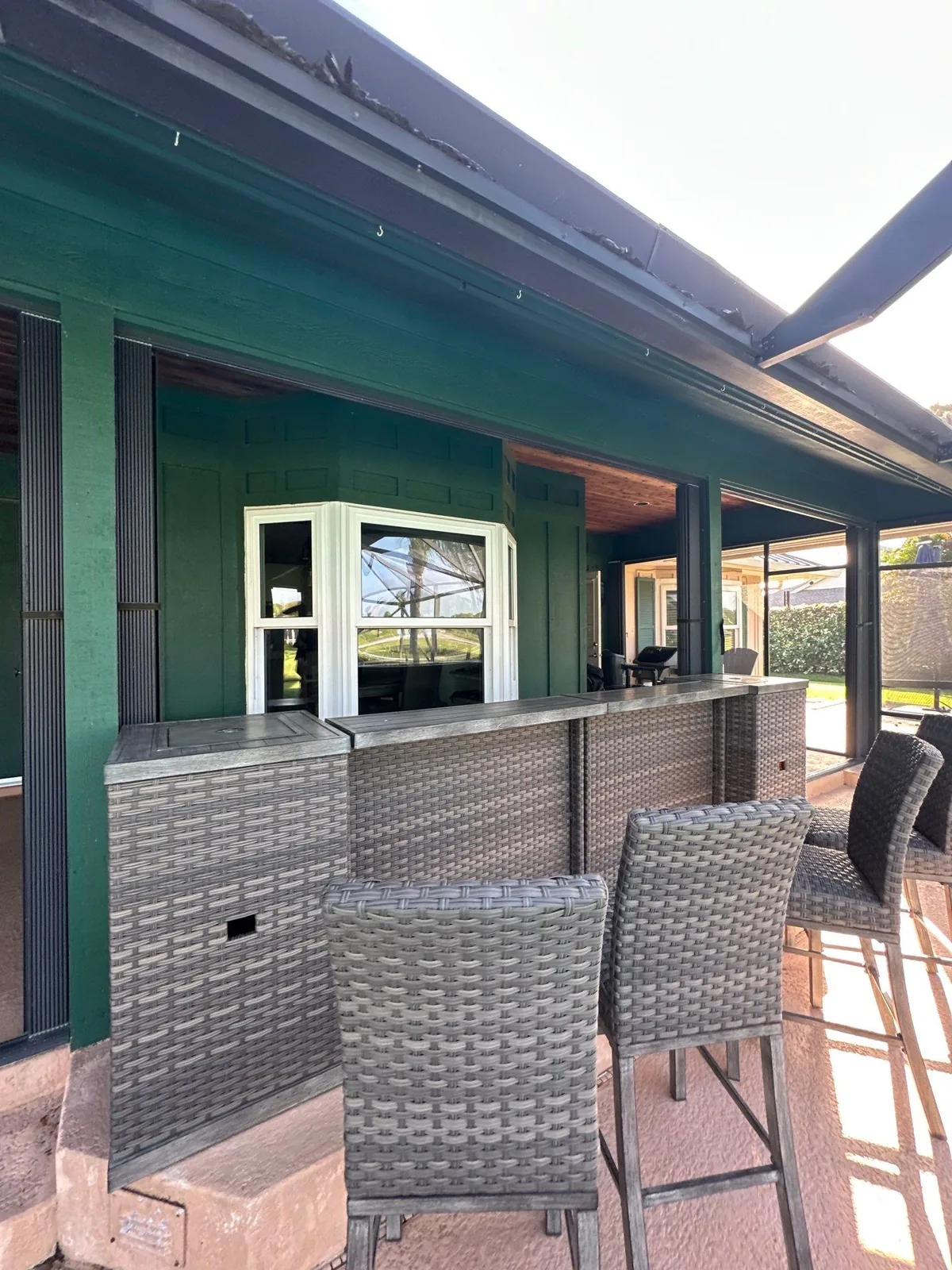 Exterior Painting in Palm City, Florida. Dark green painted exterior with white window trim above an outdoor bar counter and wicker stools.
