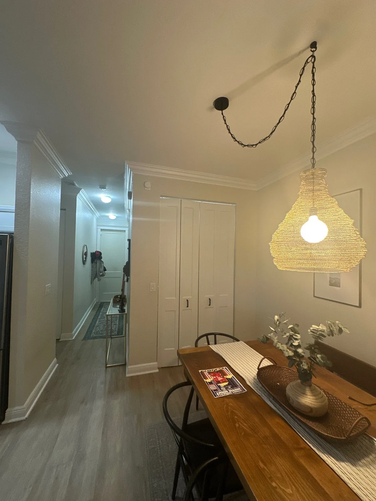 Interior Painting in Palm City, Florida. Dining area with a wood table, woven pendant light, white bi-fold closet doors and white trim, looking down a hallway.