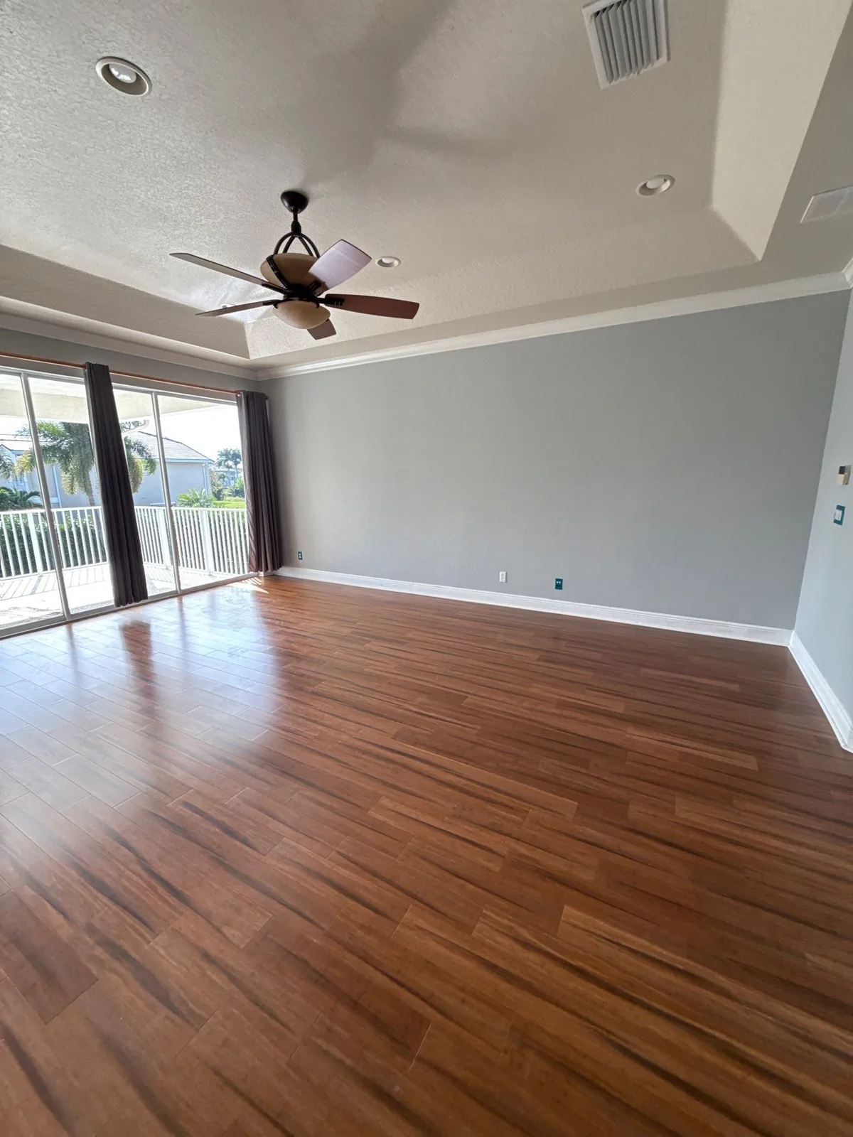 Interior Painting in Palm City, Florida. Empty living room with gray walls, white tray ceiling and wood floor, sliding glass door to a patio.