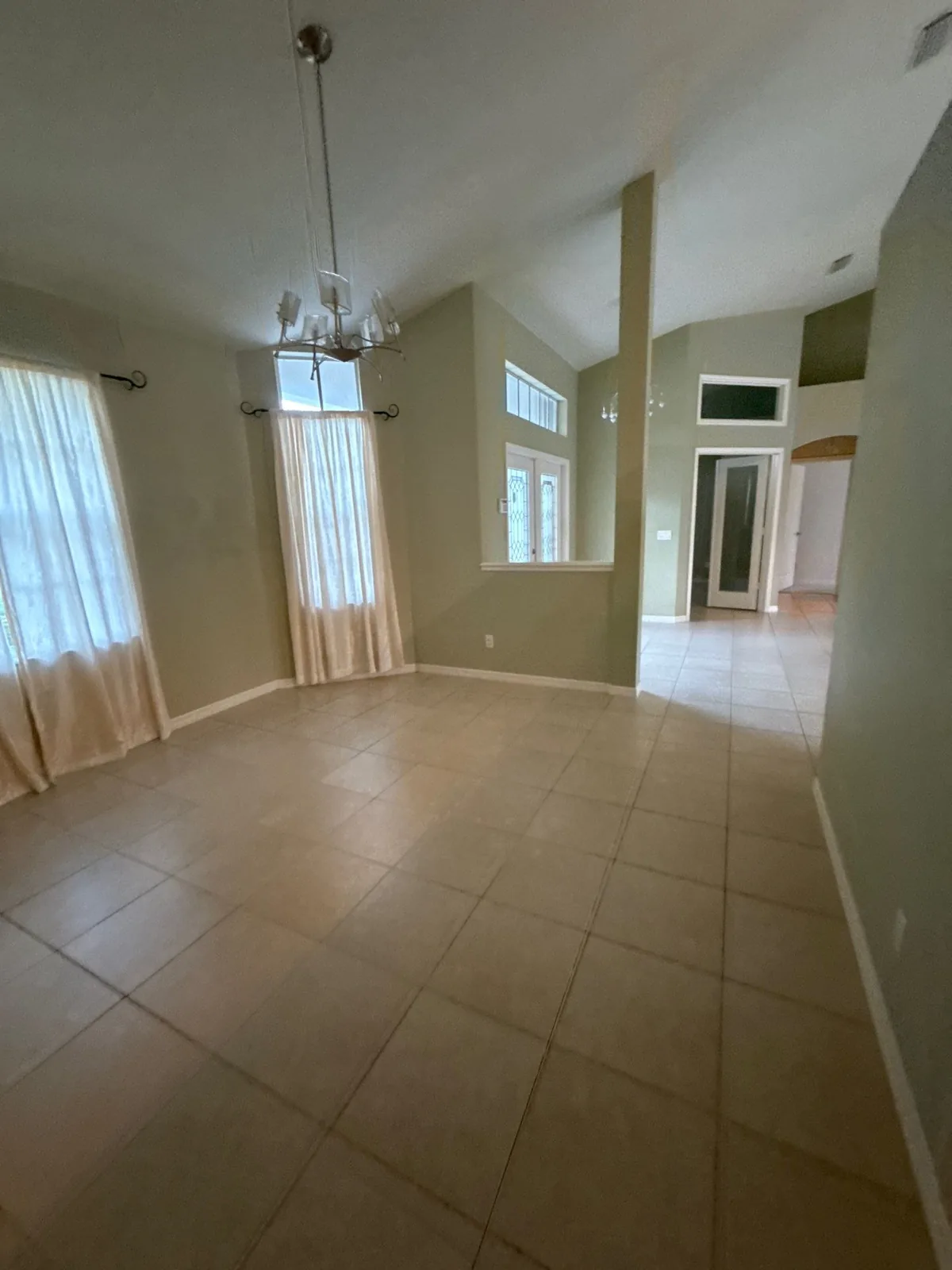 Interior Painting in Palm City, Florida. Empty dining room with sage-green painted walls, vaulted ceiling, arched window with curtains and a hanging chandelier.