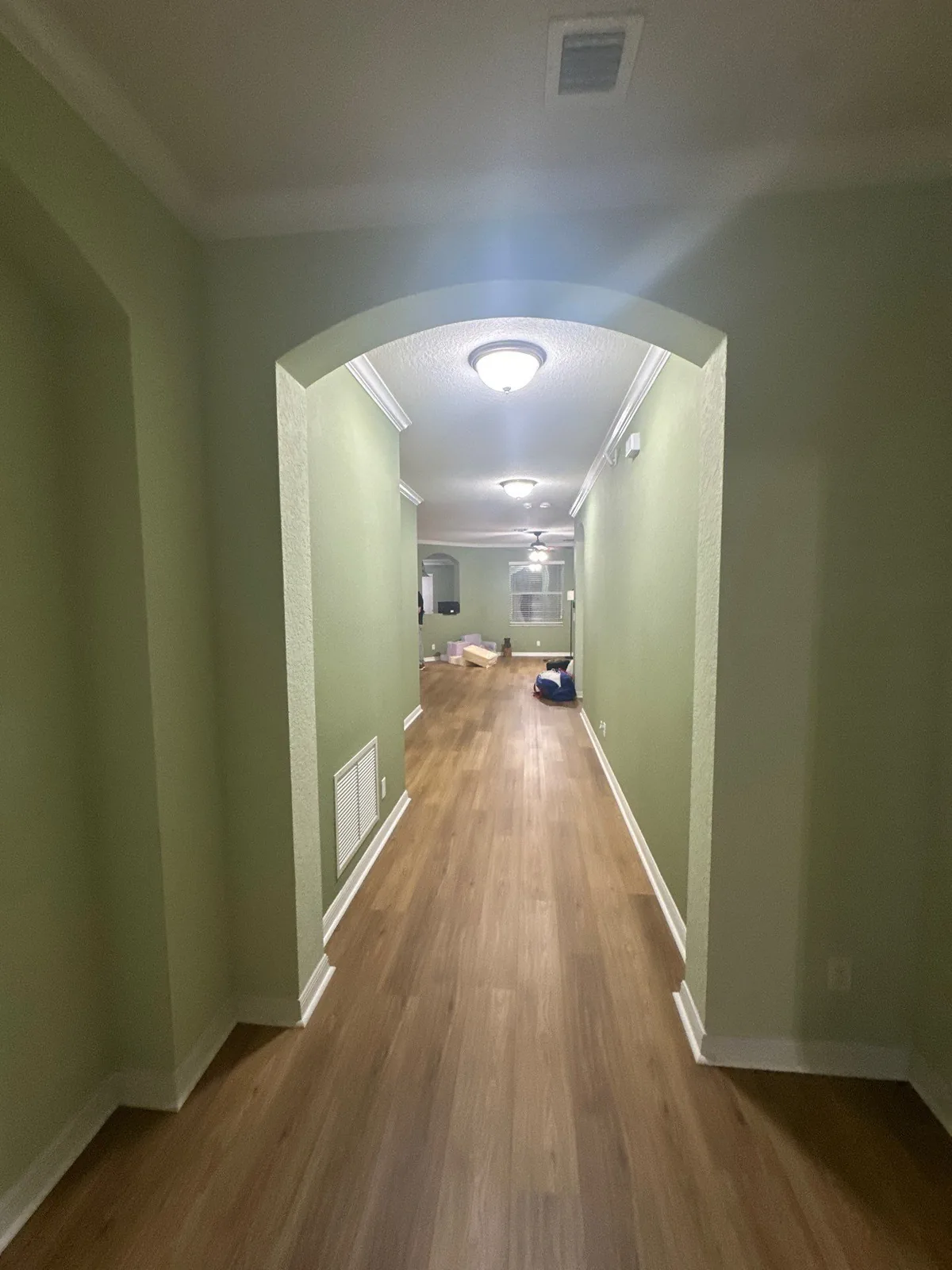 Interior Painting in Palm City, Florida. Hallway with sage green walls, white archway, crown moulding and baseboards over wood-look flooring.