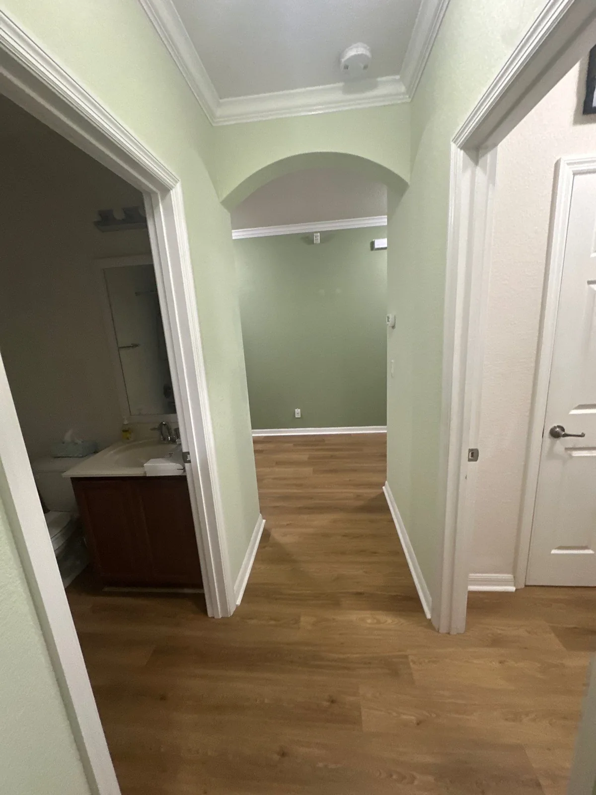 Interior Painting in Palm City, Florida. Hallway with sage green walls, white archway, crown moulding and door casings over wood-look flooring.