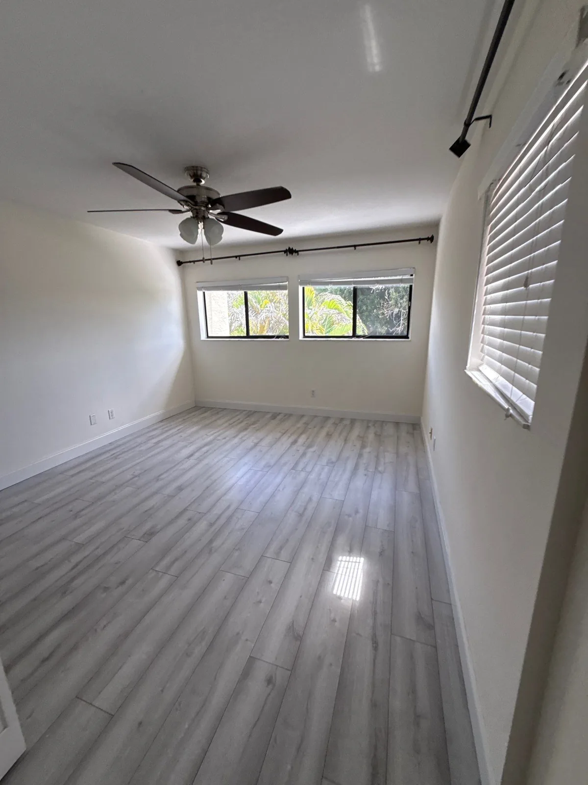 Interior Painting in Palm City, Florida. Empty bedroom with white painted walls and ceiling, a ceiling fan, two windows and wood-look plank flooring.