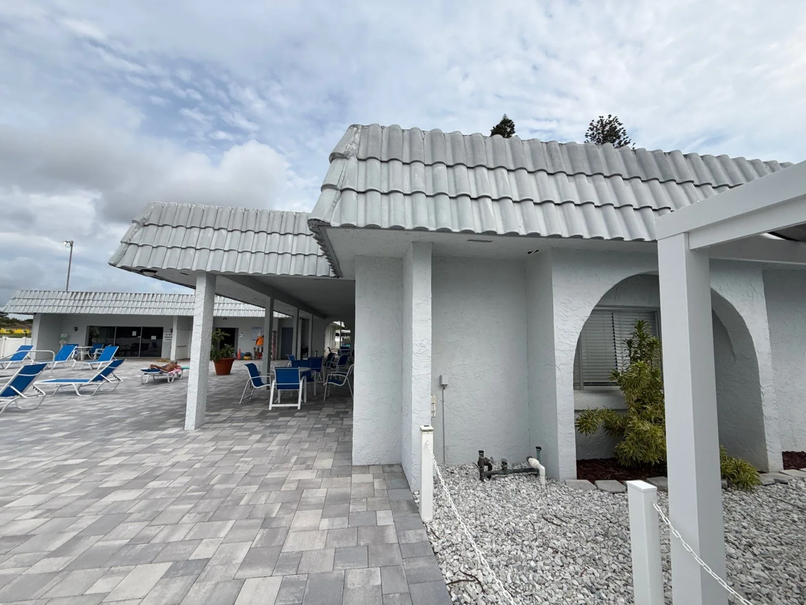 Commercial Painting in Paradise Park, Florida. White painted exterior of a single-storey tile-roofed building beside a paver pool deck with blue lounge chairs.