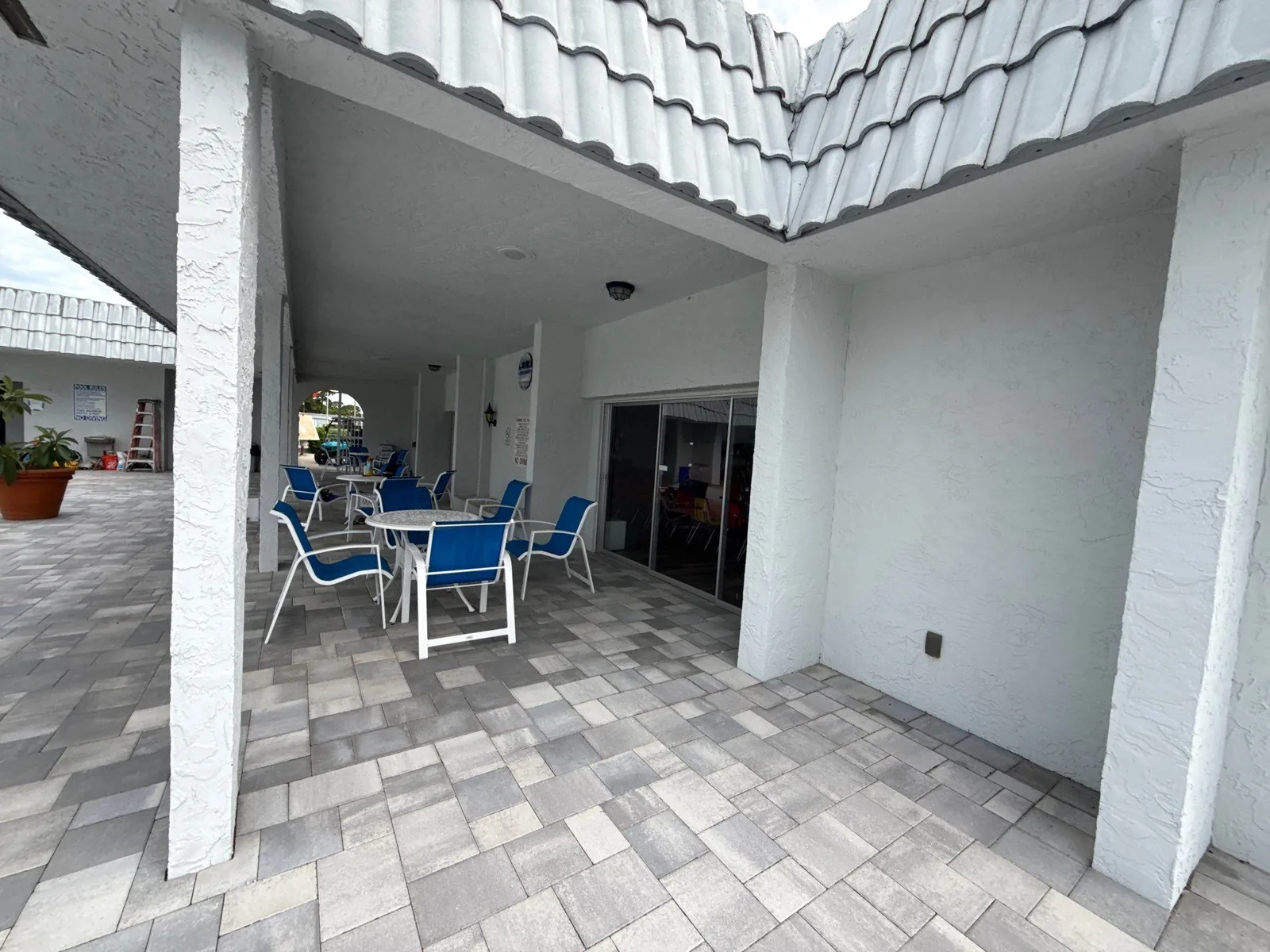 Commercial Painting in Paradise Park, Florida. Covered breezeway with white painted stucco columns and ceiling, a paver floor and blue patio chairs.