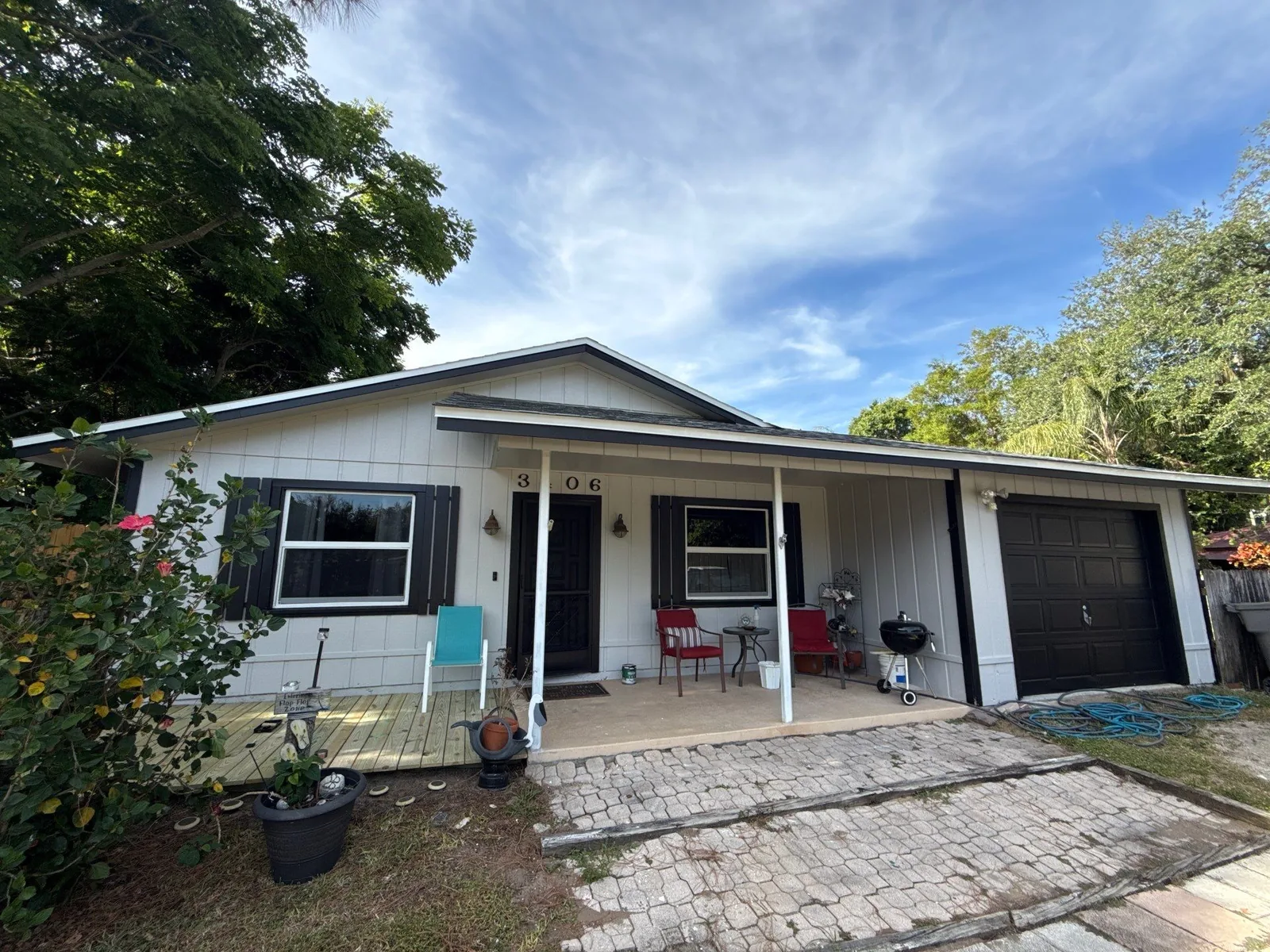 Exterior Painting in Poinciana Park, Florida. Single-storey home exterior with white board-and-batten siding, dark brown trim, covered porch and dark garage door.