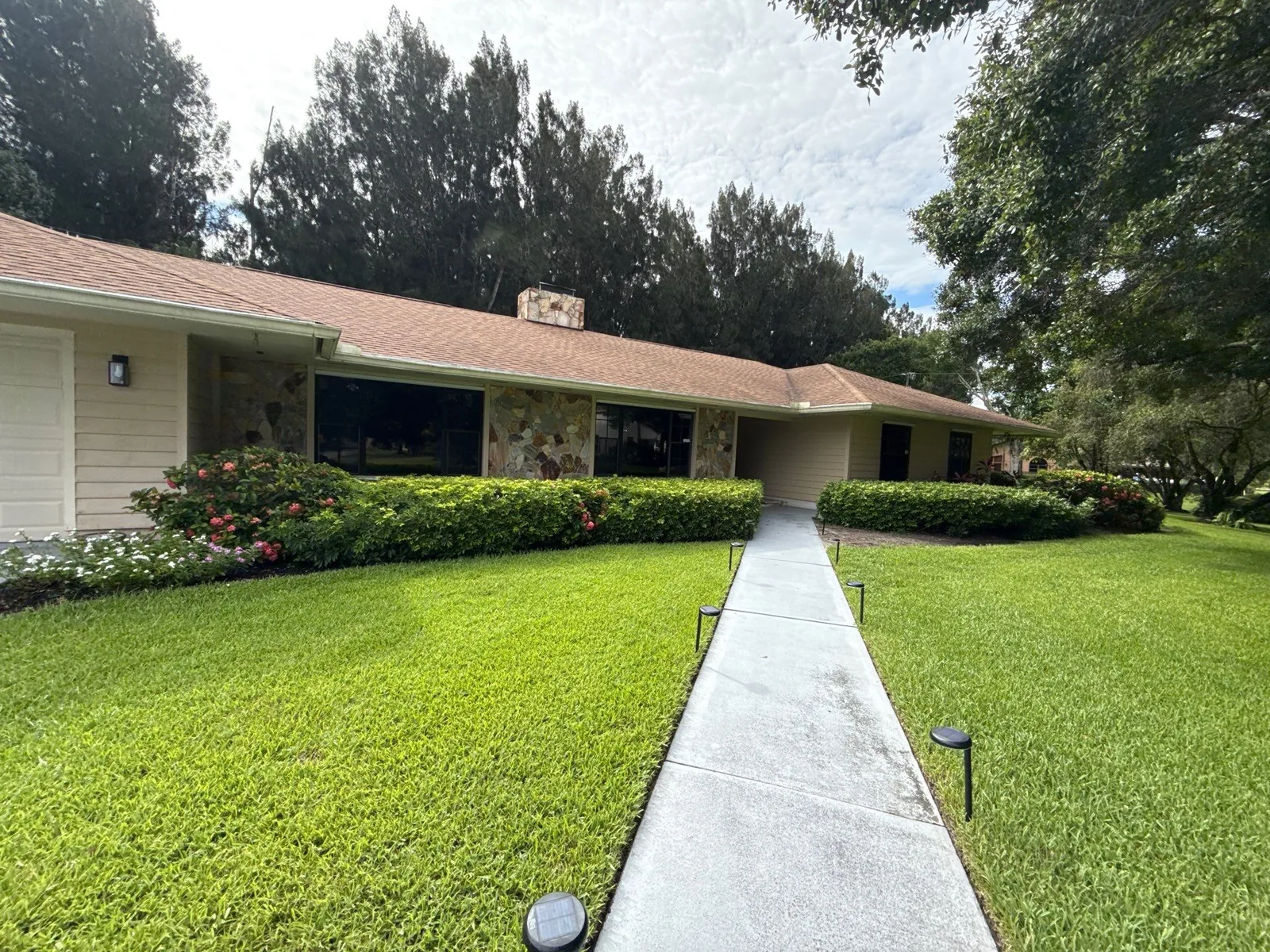 Exterior Painting in Poinciana Park, Florida. Single-storey home with stone and stucco facade, white fascia and trim, front lawn and concrete walkway.