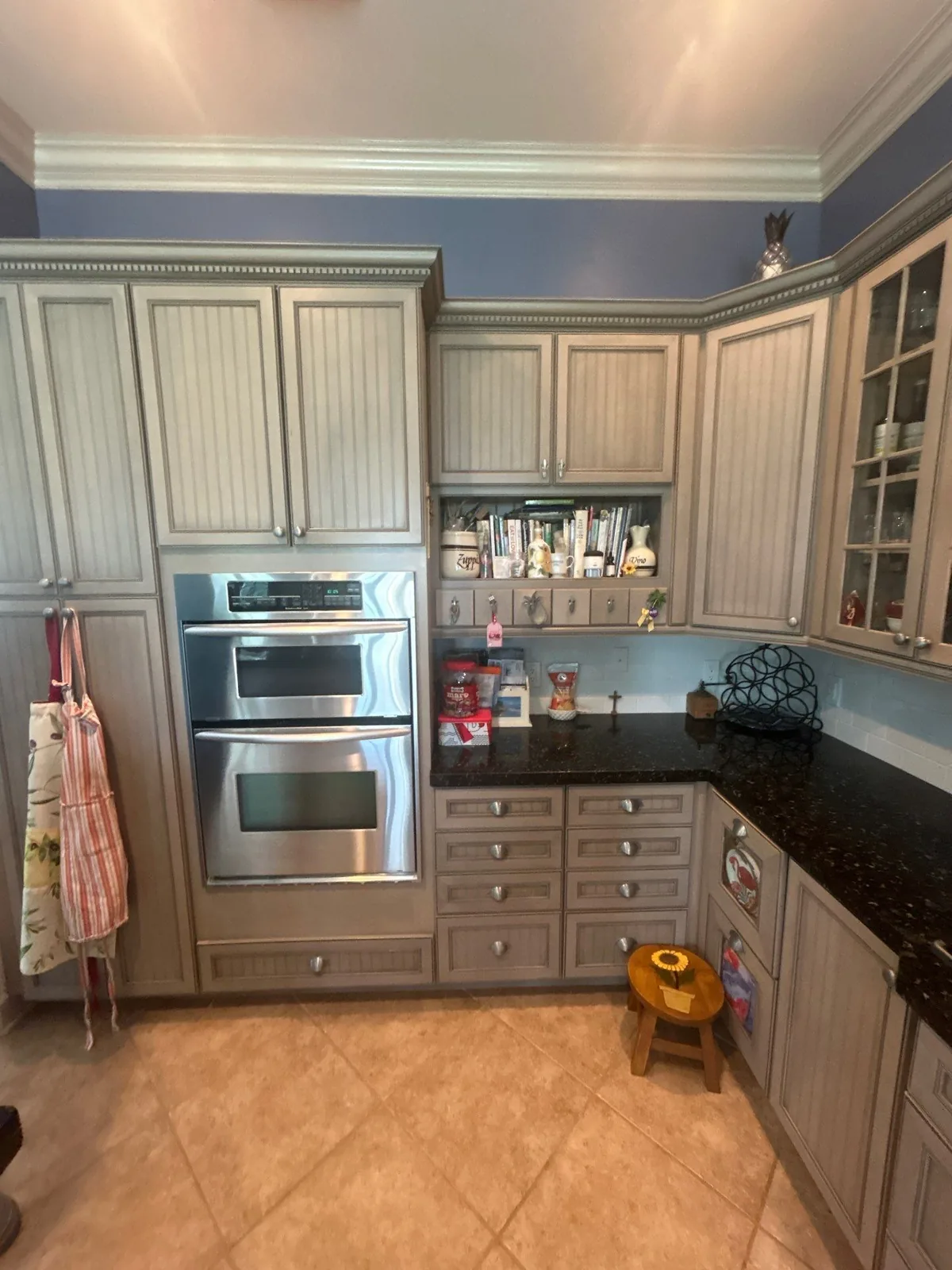 Cabinet Refinishing in Pointe West, Florida. Kitchen wall of taupe glazed cabinets with a stainless double wall oven, dark granite counter and blue walls.