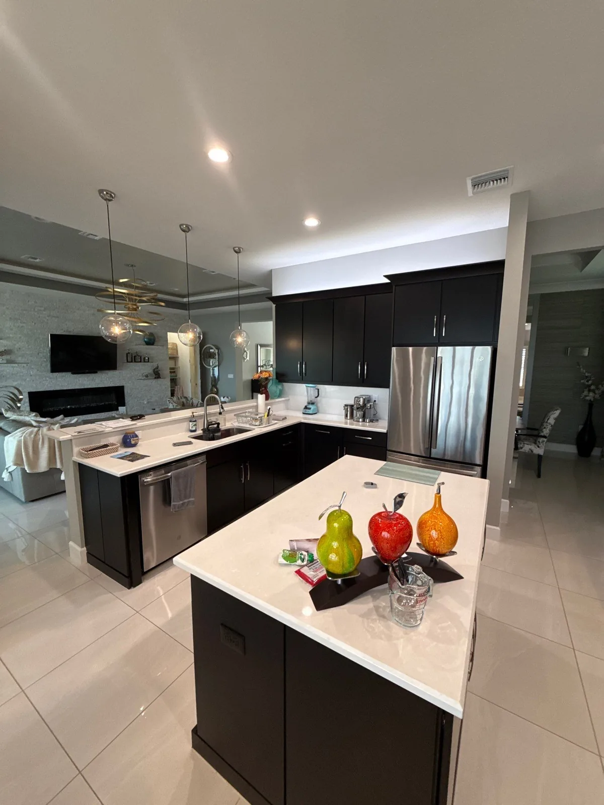 Cabinet Refinishing in Port Saint Lucie, Florida. Wide view of a kitchen with dark espresso-finish cabinets, white quartz peninsula and countertops, mirrored backsplash and stainless refrigerator.