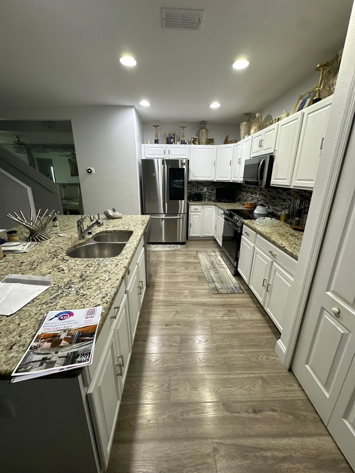 Cabinet Refinishing in Port Saint Lucie, Florida. Galley kitchen with white cabinets, speckled granite countertops, stainless refrigerator and range, wood-look plank flooring.