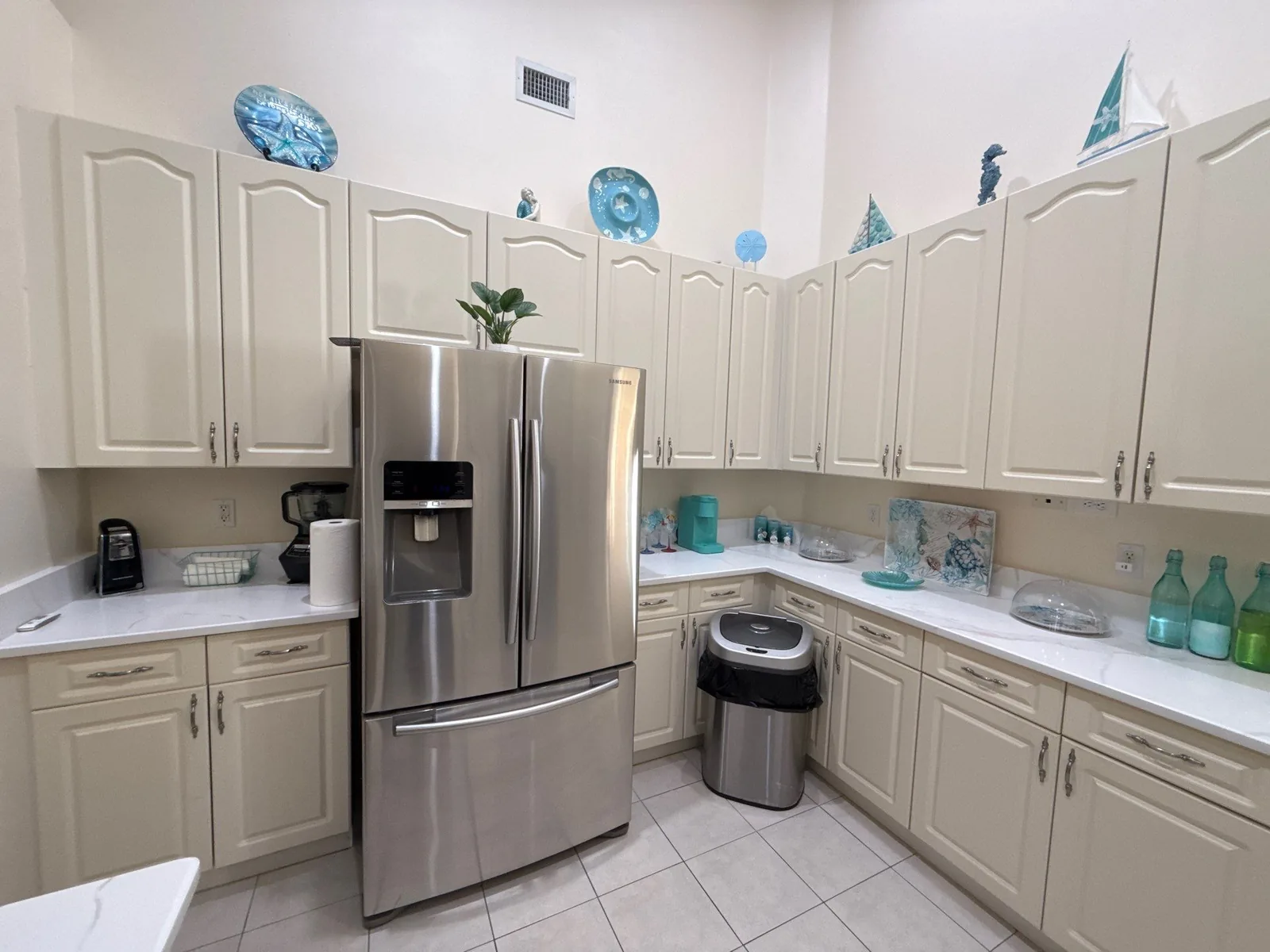 Cabinet Refinishing in Port Saint Lucie, Florida. Kitchen with cream-painted arch-panel cabinets, stainless steel refrigerator and light stone countertops.