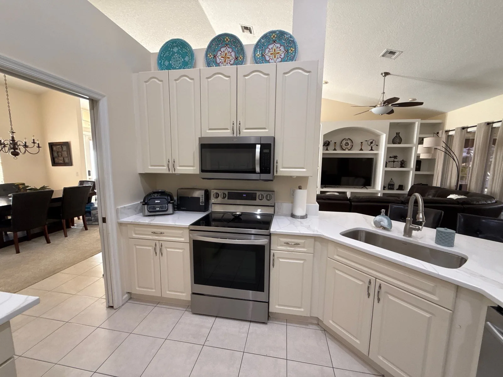 Cabinet Refinishing in Port Saint Lucie, Florida. Kitchen with off-white painted cabinets, stainless range and over-range microwave, light stone countertops, open to a dining area.