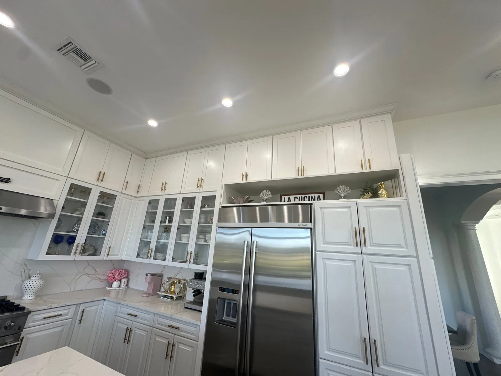 Cabinet Refinishing in Port Saint Lucie, Florida. White kitchen cabinets with glass-front uppers and gold hardware flanking a stainless refrigerator.