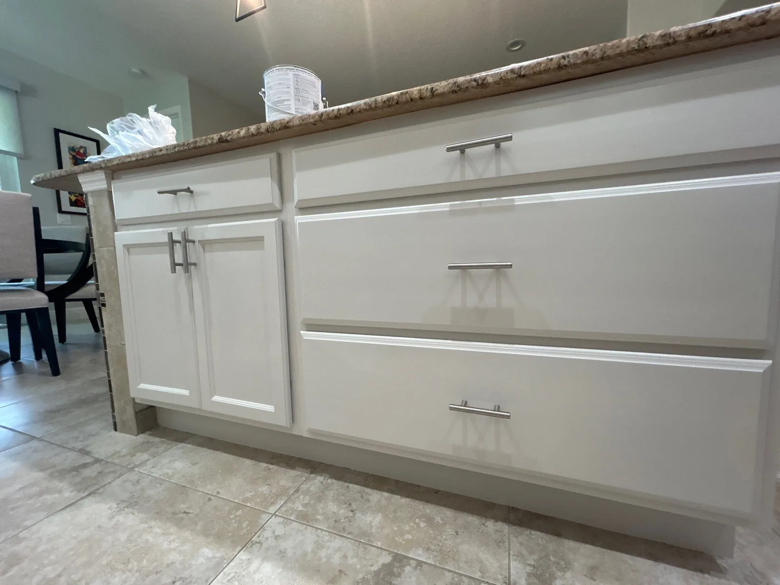 Cabinet Refinishing in Port Saint Lucie, Florida. White refinished kitchen island with shaker-style doors and three deep drawers, brushed nickel bar pulls and a granite countertop.