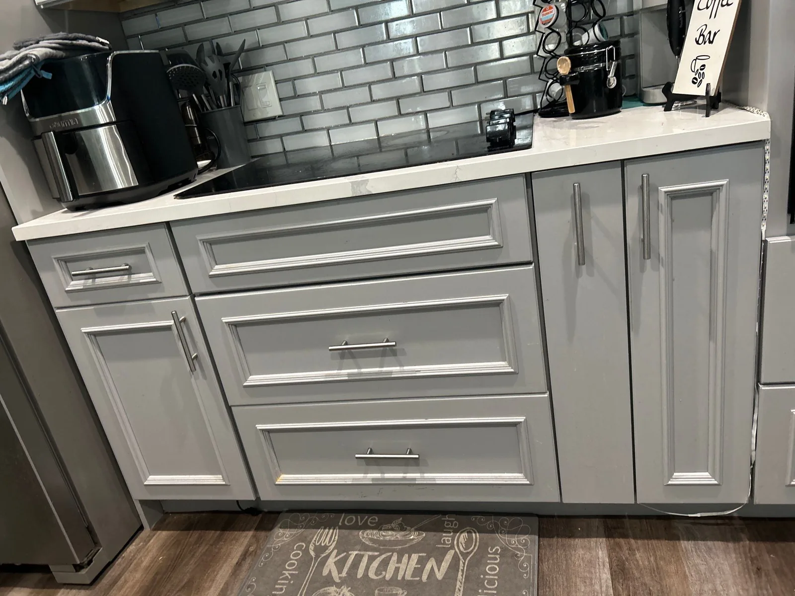 Cabinet Refinishing in Port Saint Lucie, Florida. Grey refinished base cabinets and drawer fronts with chrome bar pulls, white counter and grey tile backsplash.