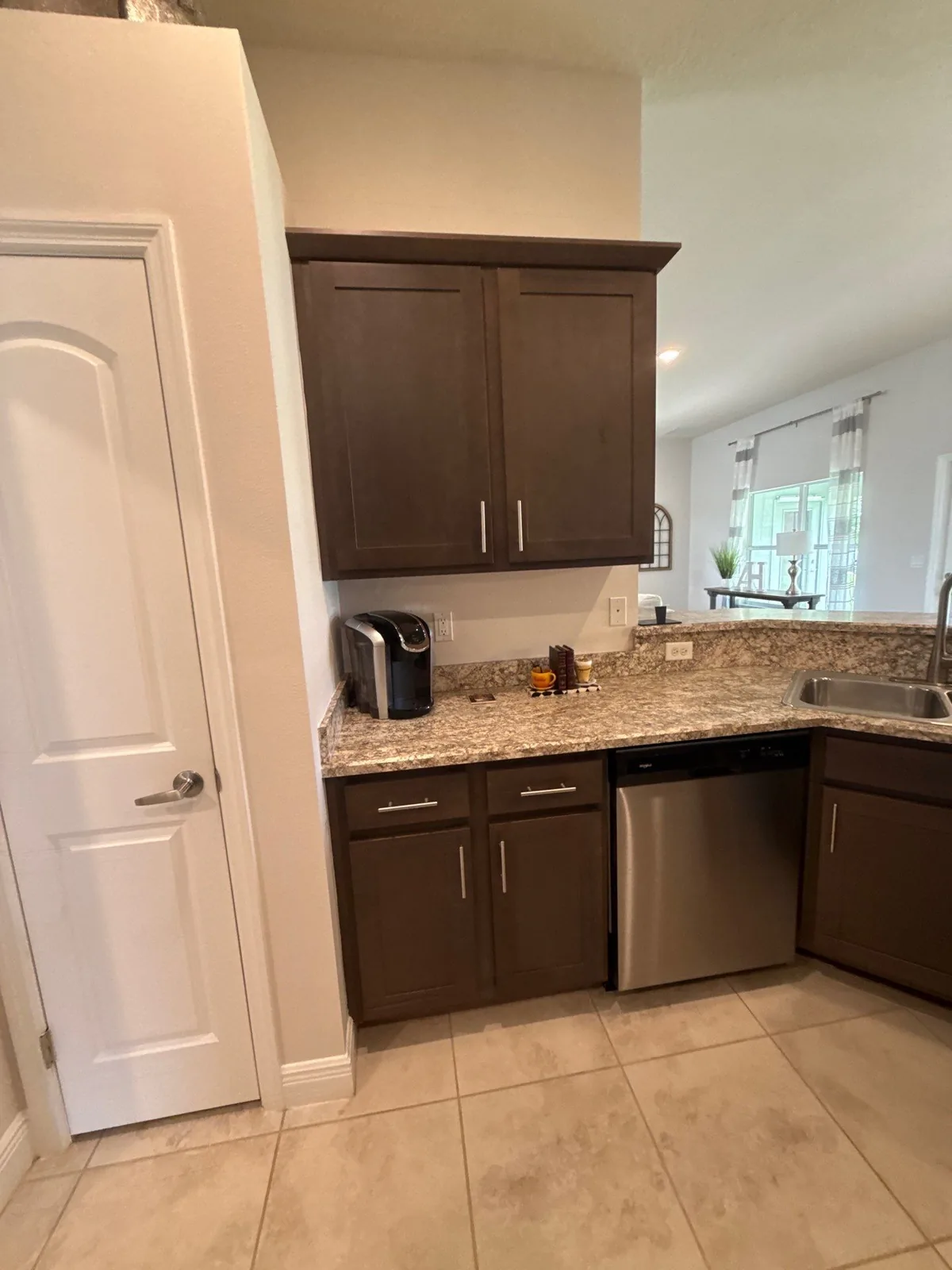Cabinet Refinishing in Port Saint Lucie, Florida. Kitchen corner with dark brown cabinets, speckled granite counters, a stainless dishwasher and a white pantry door.