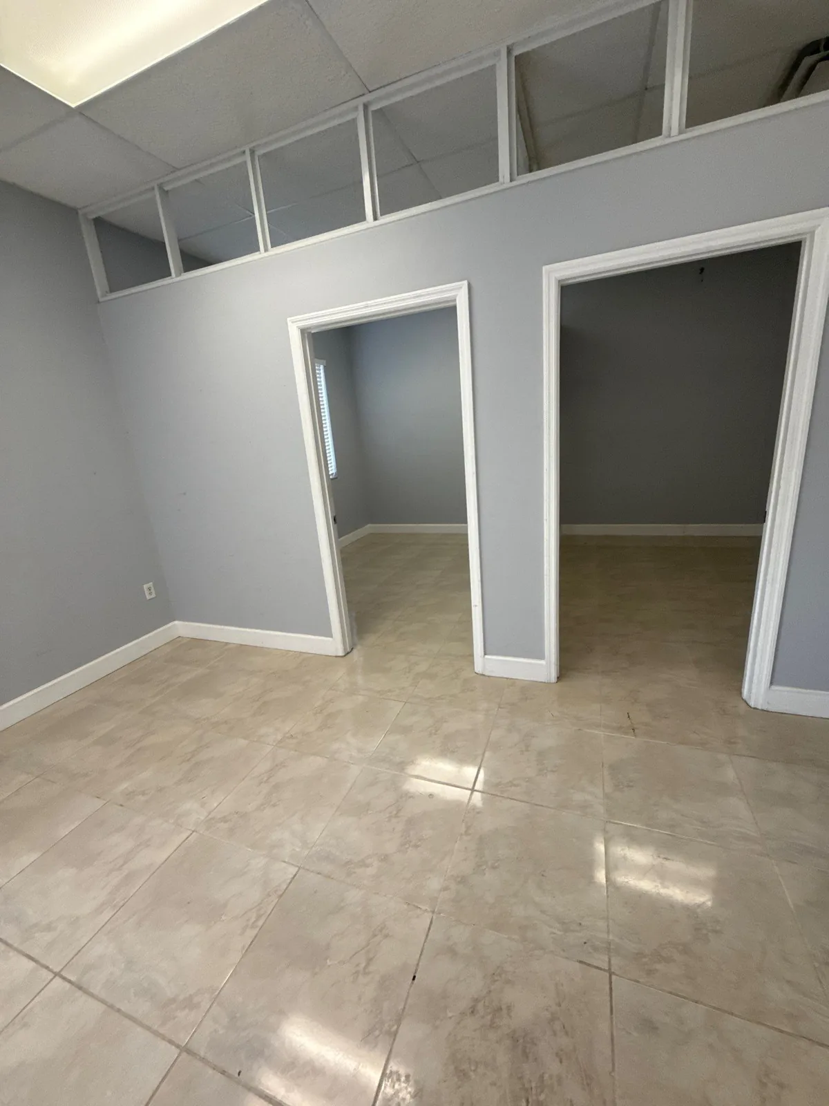Commercial Painting in Port Saint Lucie, Florida. Empty commercial interior with grey walls, crisp white door casings and baseboards, two open doorways and large tile flooring.