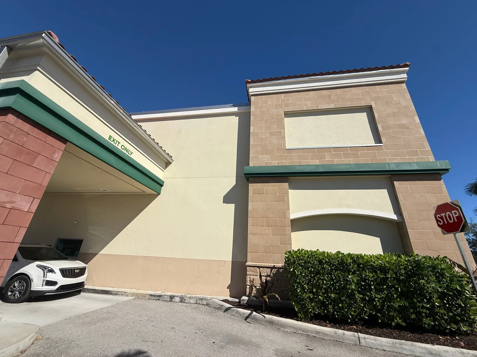 Commercial Painting in Port Saint Lucie, Florida. Commercial plaza exterior with beige and tan stucco walls, green fascia trim and hedges under a clear sky.