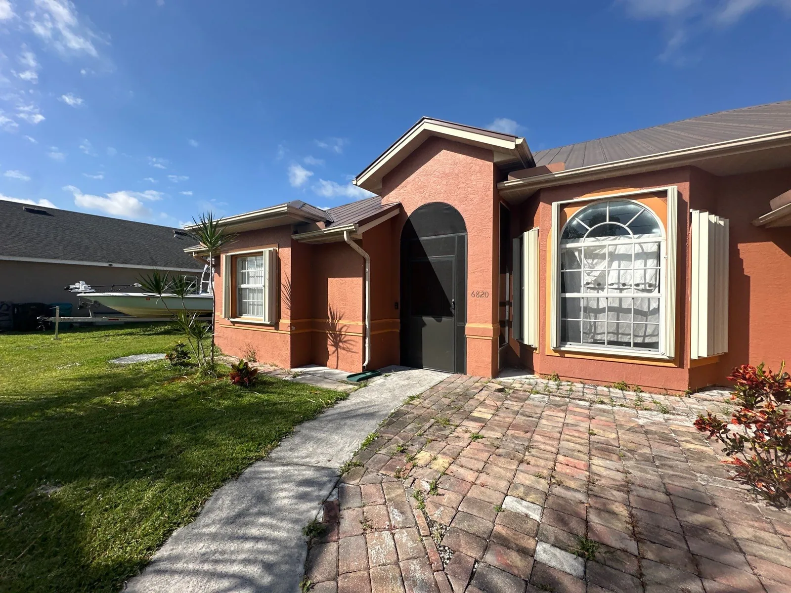 Exterior Painting in Port Saint Lucie, Florida. Front elevation of single-storey stucco home in terracotta with lighter trim, arched picture window and paver walkway.