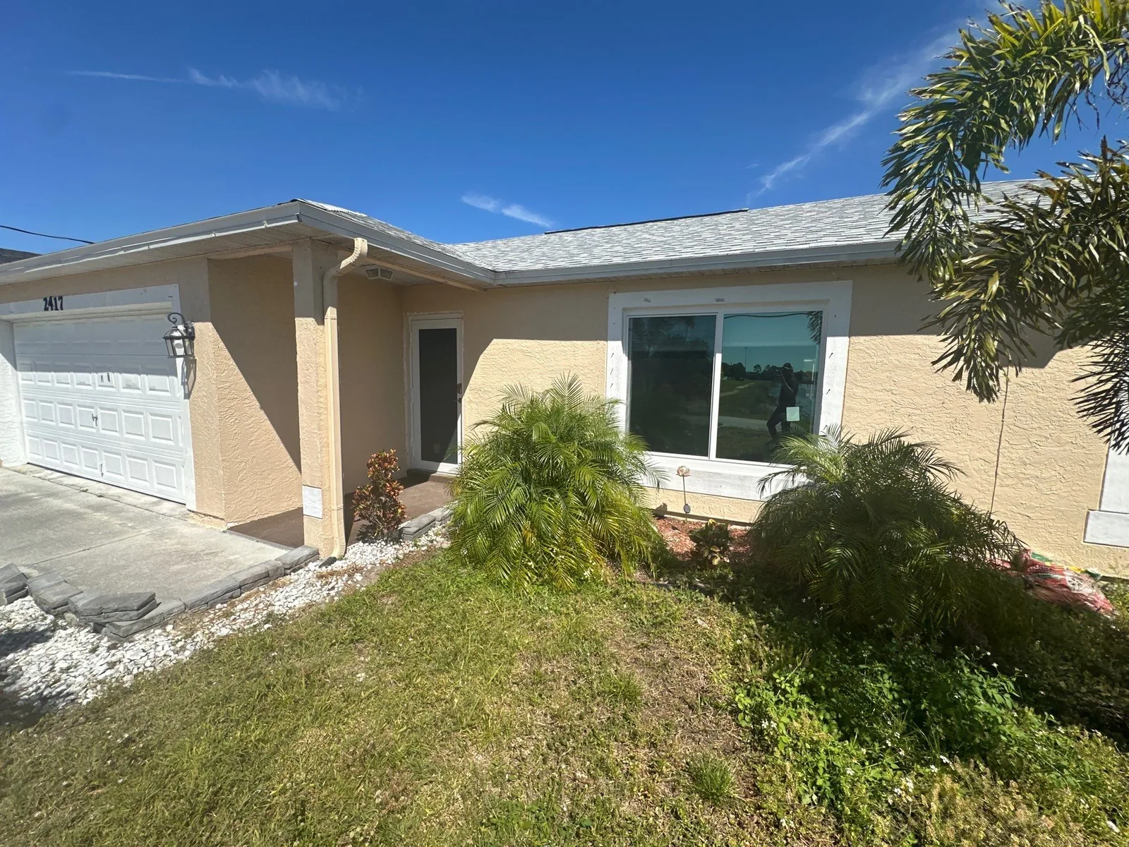 Exterior Painting in Port Saint Lucie, Florida. Front elevation of a single-storey yellow stucco house with white garage door, white trim and a picture window.