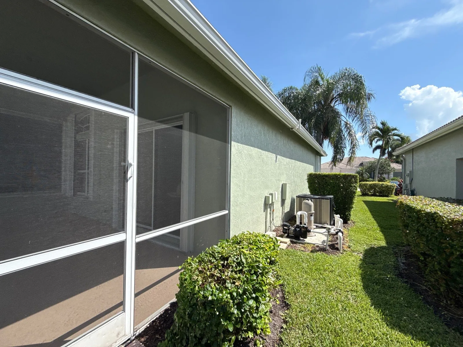 Exterior Painting in Port Saint Lucie, Florida. Single-storey home side elevation, light green stucco with white trim and a screened lanai.