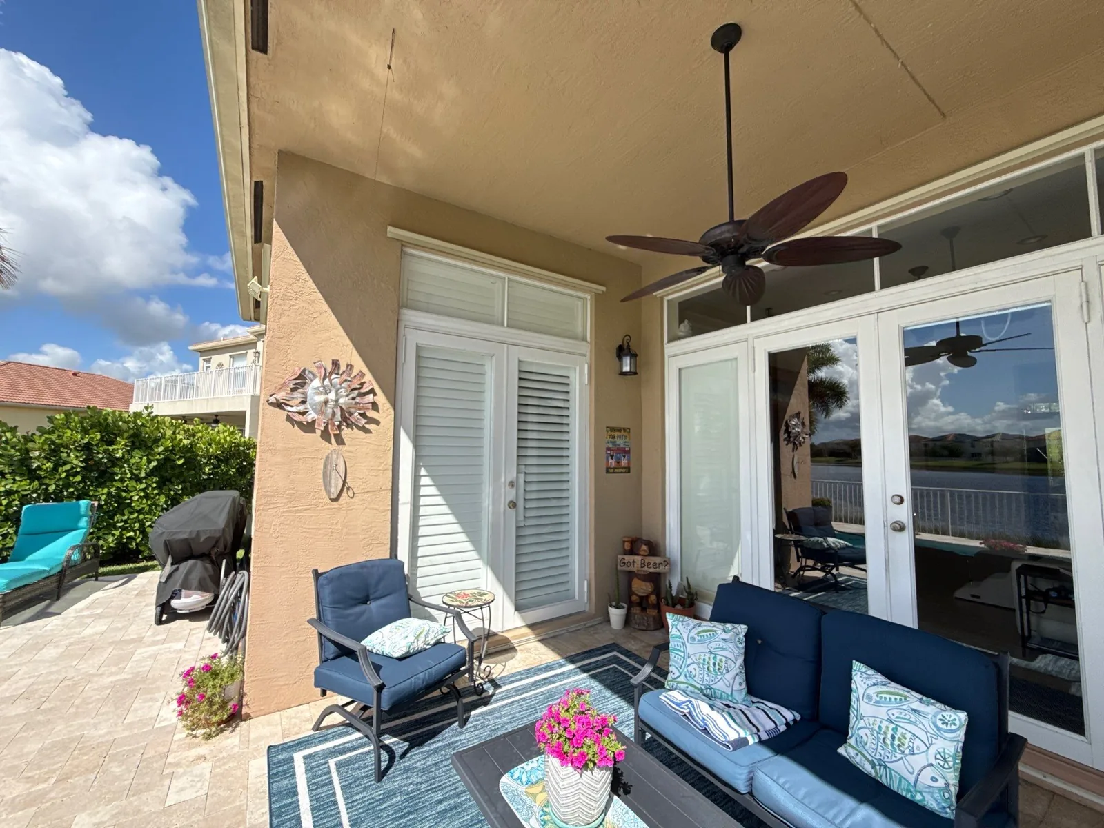 Exterior Painting in Port Saint Lucie, Florida. Covered patio with tan stucco walls and painted ceiling, white louvered door and french doors, two ceiling fans and outdoor seating.