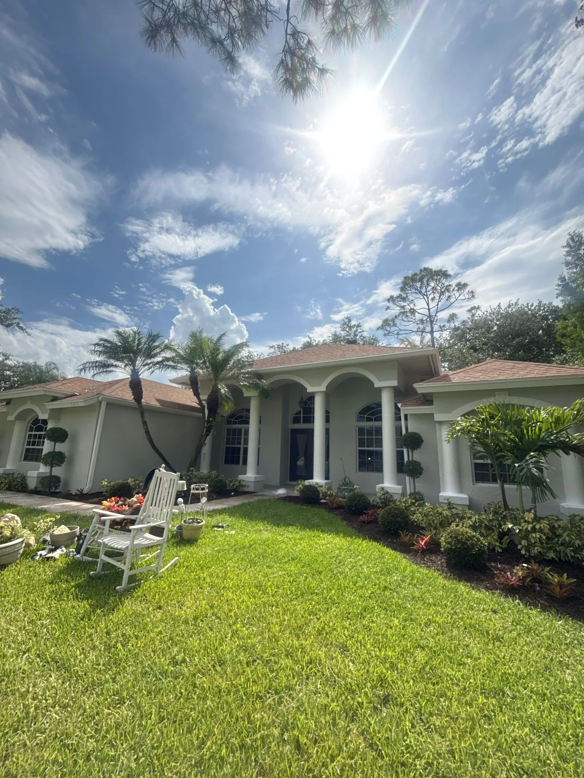Exterior Painting in Port Saint Lucie, Florida. Single-storey stucco home painted white with an arched columned entry, tile roof, palm tree and a green front lawn.