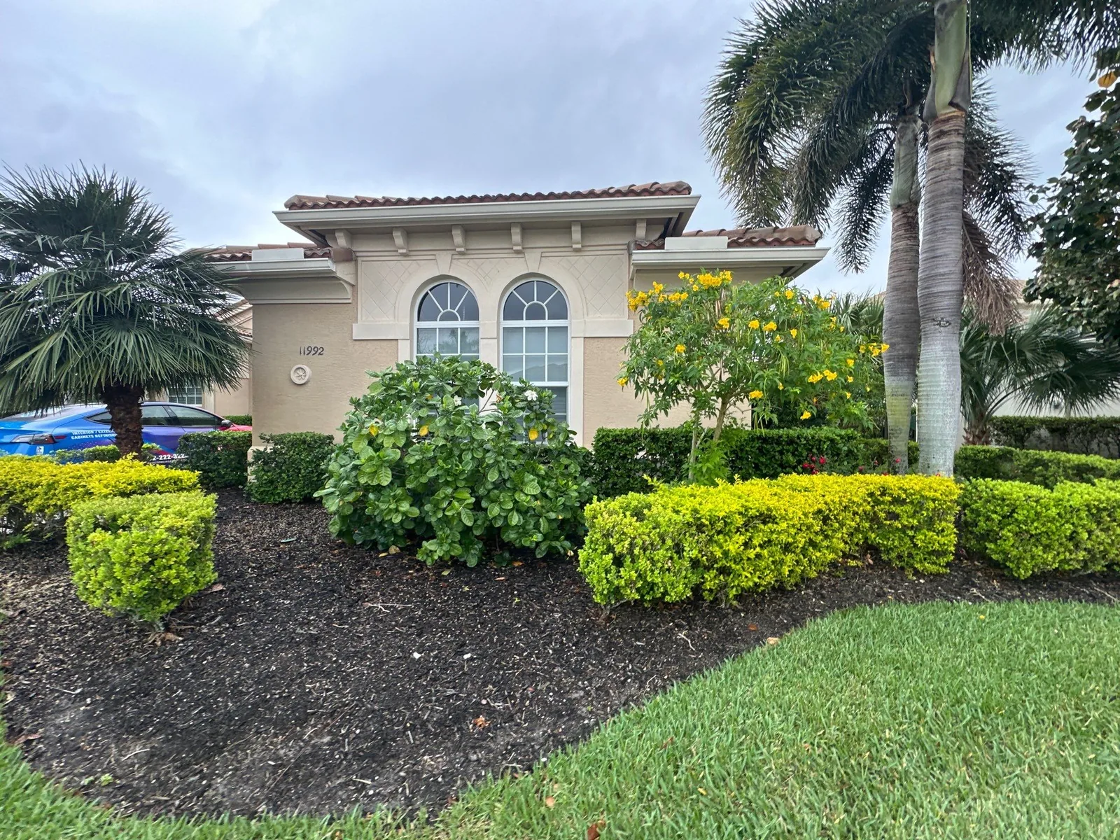 Exterior Painting in Port Saint Lucie, Florida. Front elevation of a cream stucco home with barrel tile roof, twin arched windows and mature landscaping.