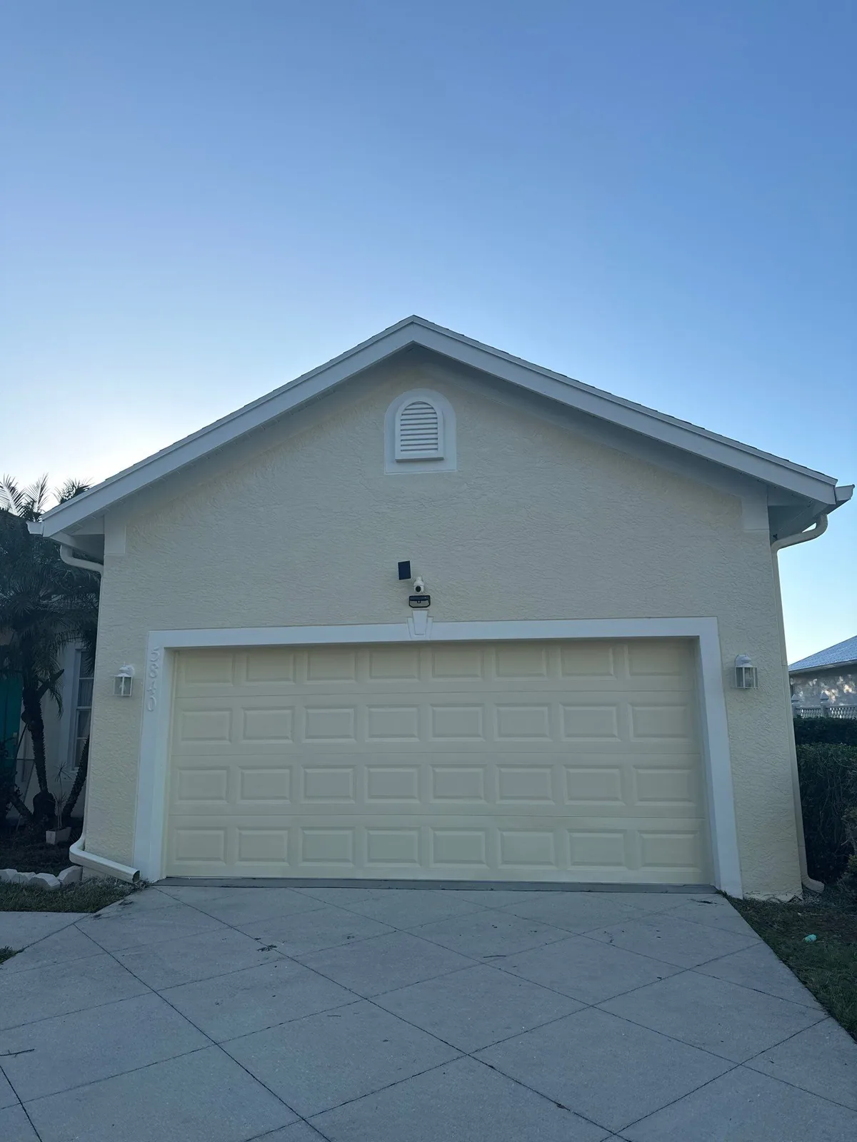 Exterior Painting in Port Saint Lucie, Florida. Two-car garage on a pale yellow stucco home with white trim and a cream sectional garage door.