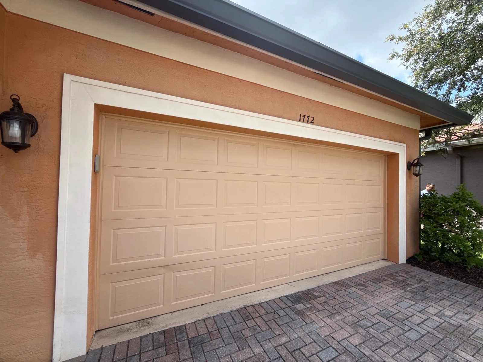 Exterior Painting in Port Saint Lucie, Florida. Attached two-car garage with tan sectional door set in terracotta stucco wall with white trim and paver driveway.