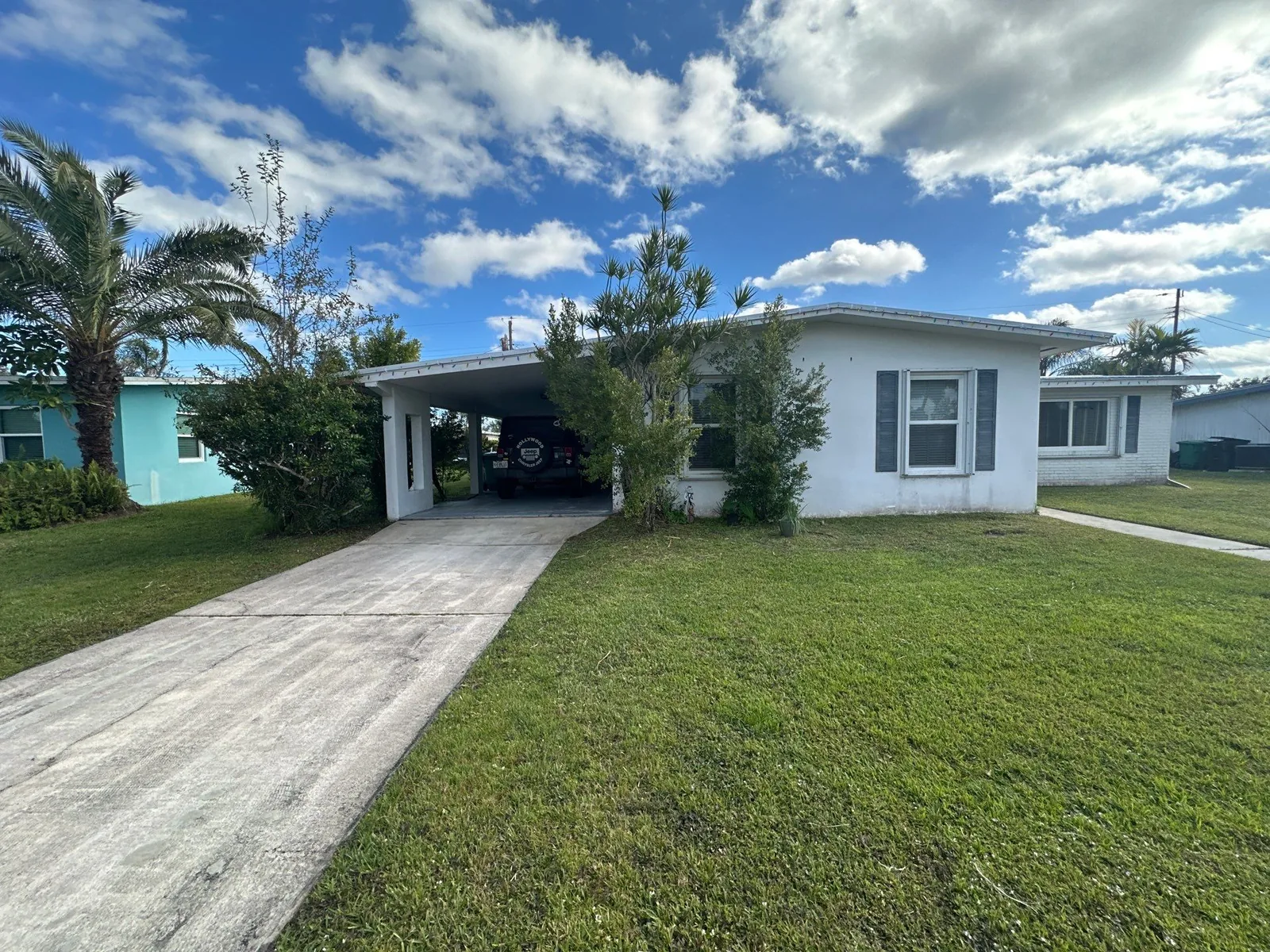 Exterior Painting in Port Saint Lucie, Florida. Single-storey house with white painted exterior, pale trim and shutters, an attached carport and a concrete driveway.