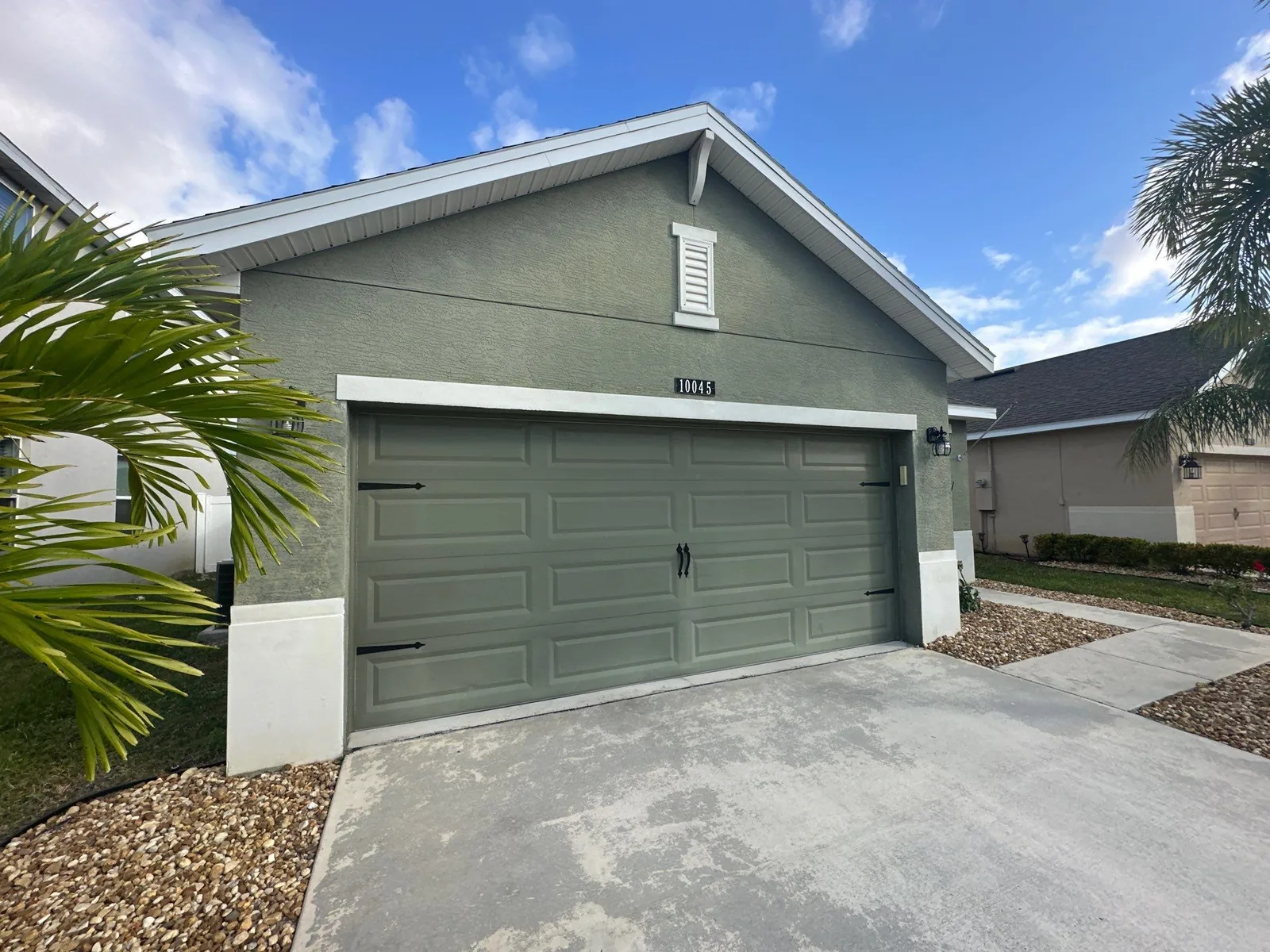 Exterior Painting in Port Saint Lucie, Florida. Single-storey stucco home painted sage green with white trim and a matching sage green sectional garage door.