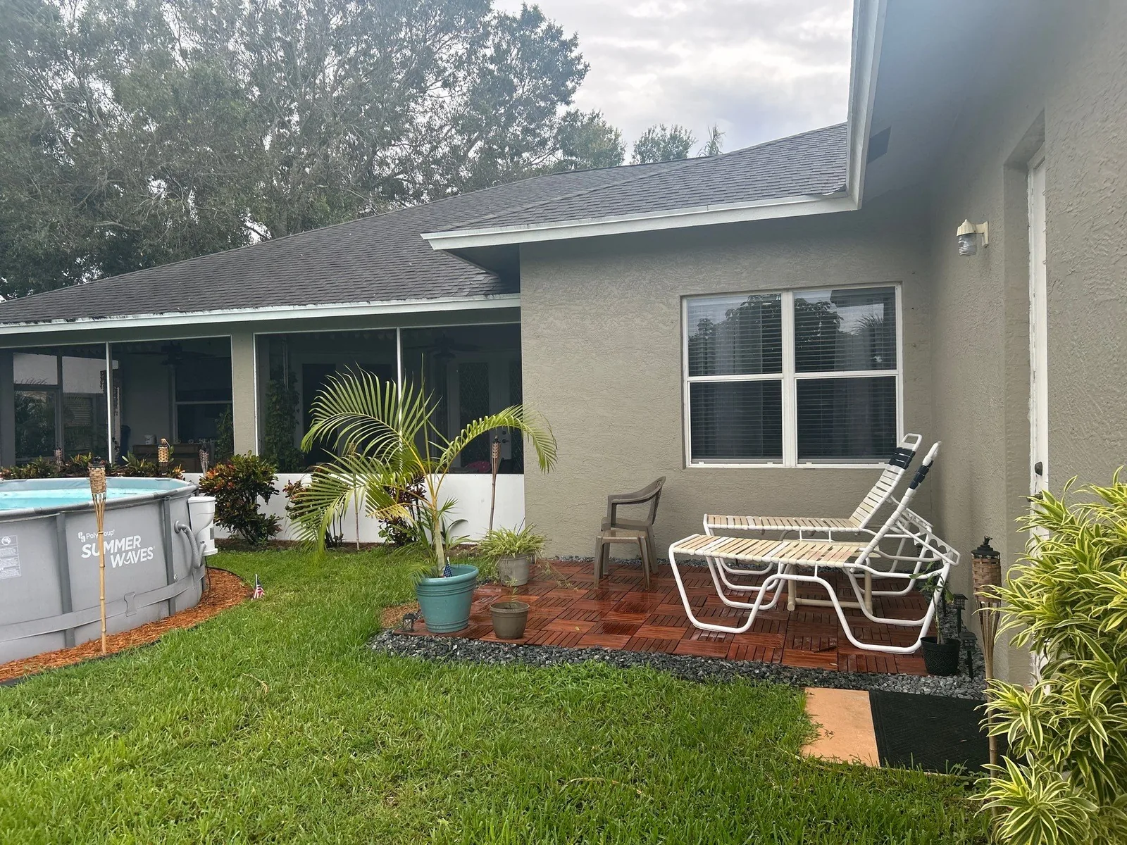 Exterior Painting in Port Saint Lucie, Florida. Rear elevation of a single-storey house, grey stucco with white window trim, patio chairs on a paver patio.