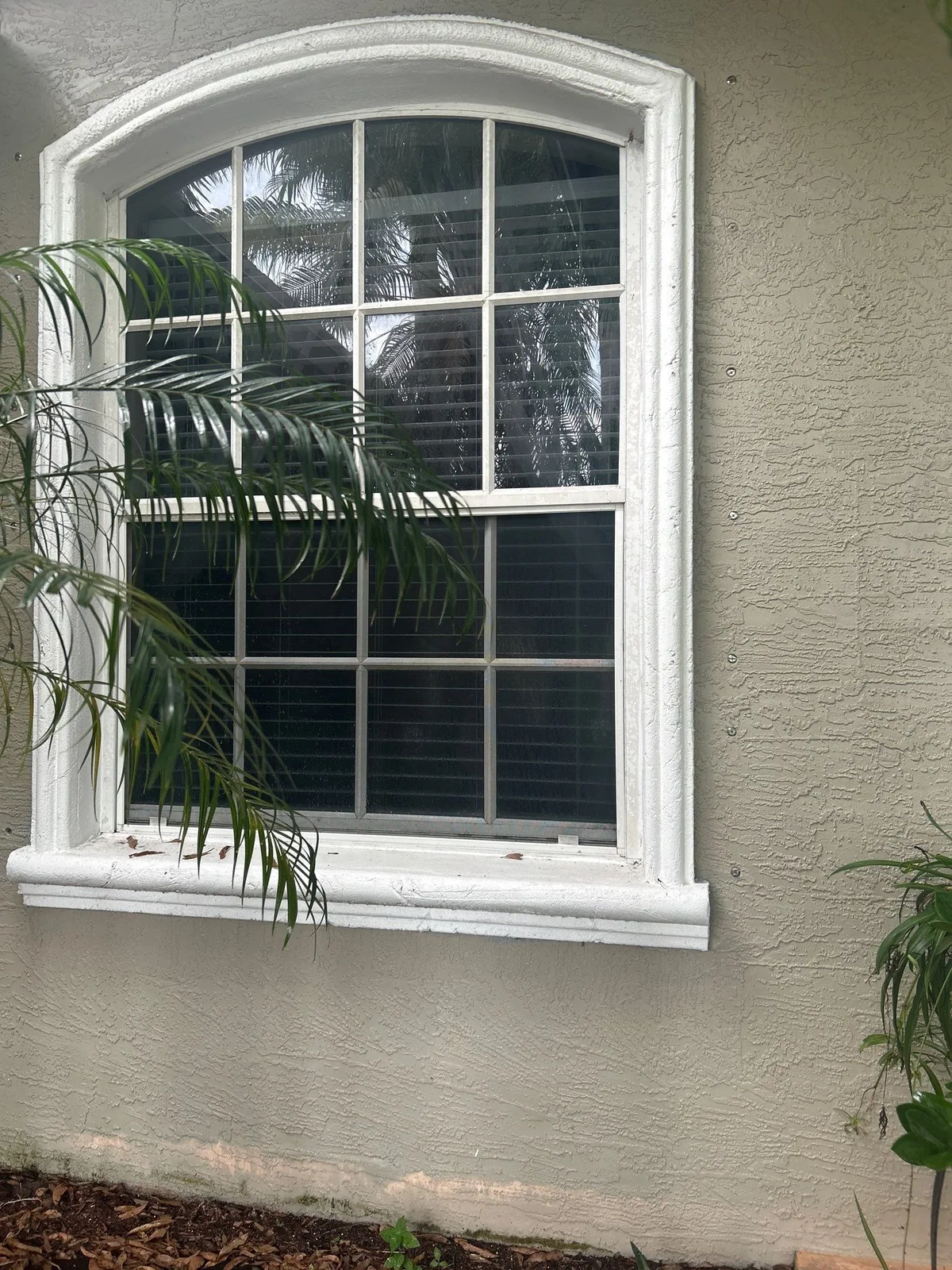 Exterior Painting in Port Saint Lucie, Florida. Arched exterior window with white trim and sill set in grey stucco wall.