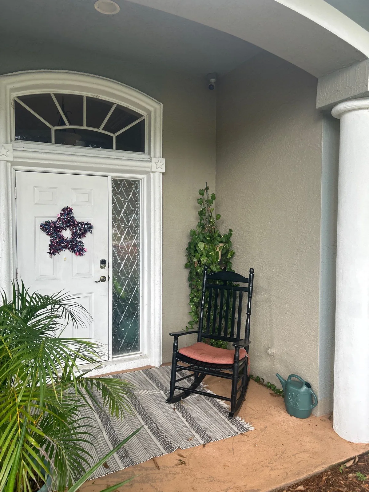 Exterior Painting in Port Saint Lucie, Florida. Covered front entry with a white front door and sidelight, grey stucco walls and a black rocking chair.