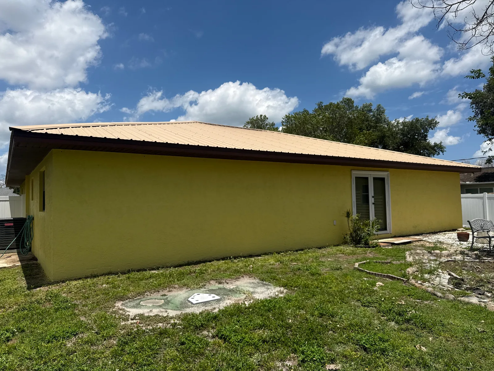 Exterior Painting in Port Saint Lucie, Florida. Rear elevation of a single-storey stucco home painted yellow with brown trim under a metal roof.