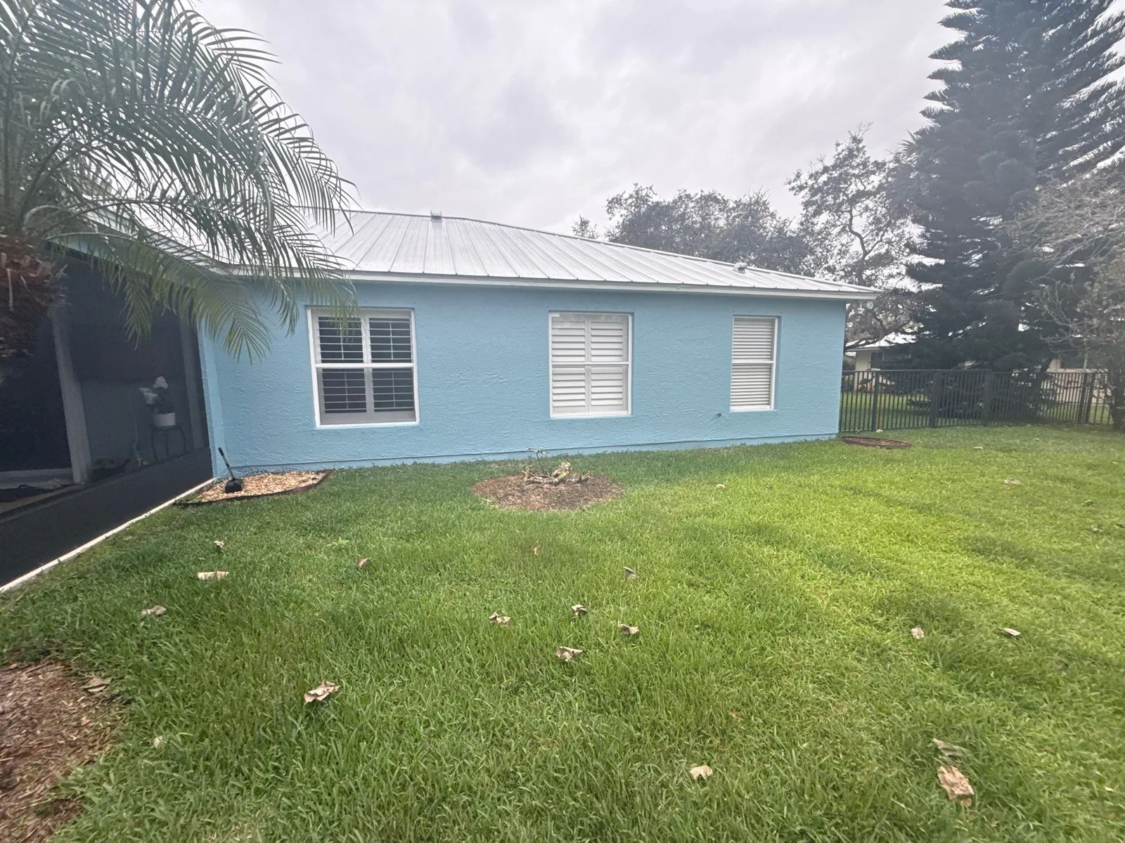 Exterior Painting in Port Saint Lucie, Florida. Single-storey house exterior, light blue stucco walls with white trim and metal roof.