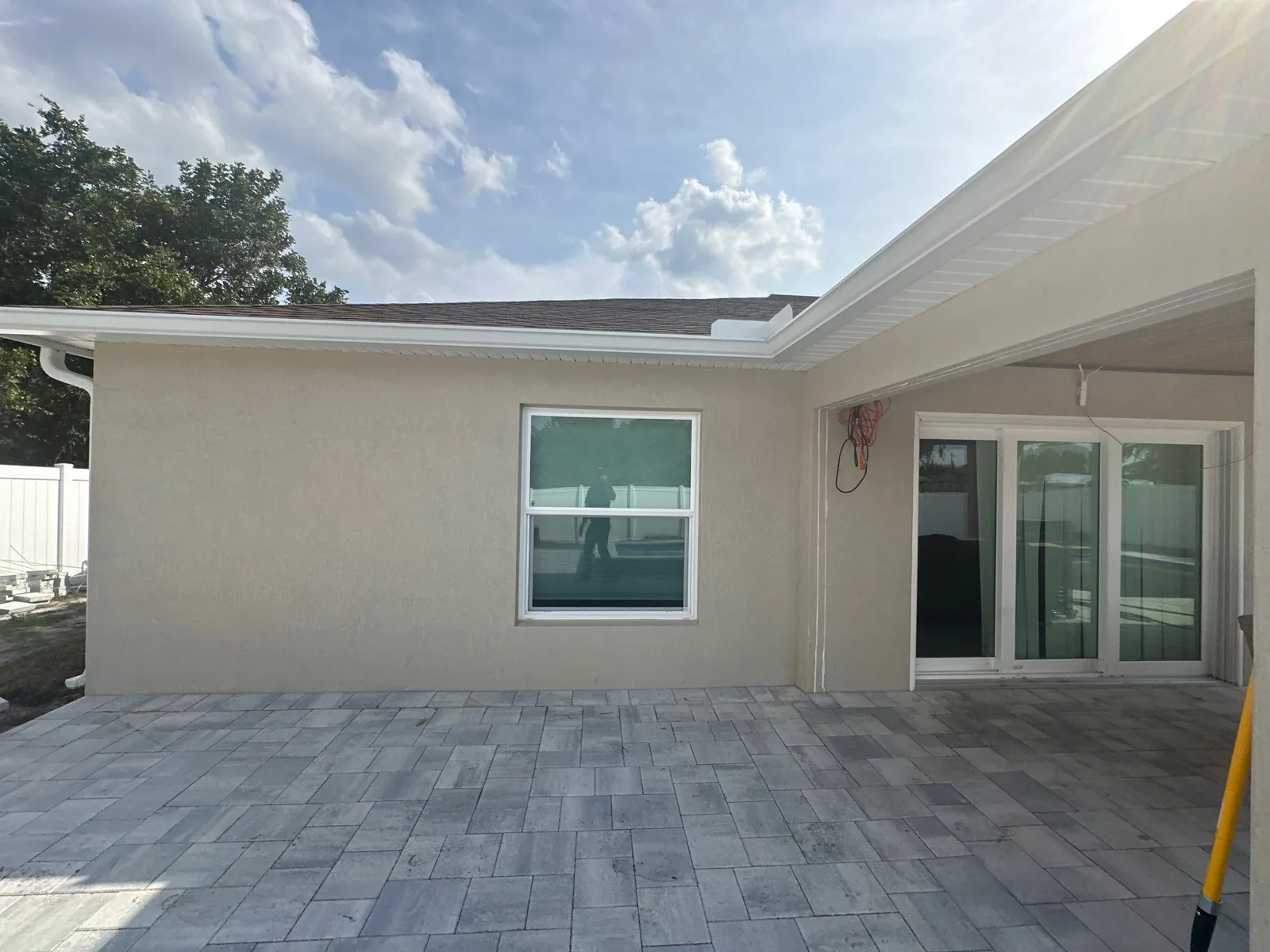 Exterior Painting in Port Saint Lucie, Florida. Rear exterior of a single-storey home, beige stucco with white soffit and fascia, paver patio.